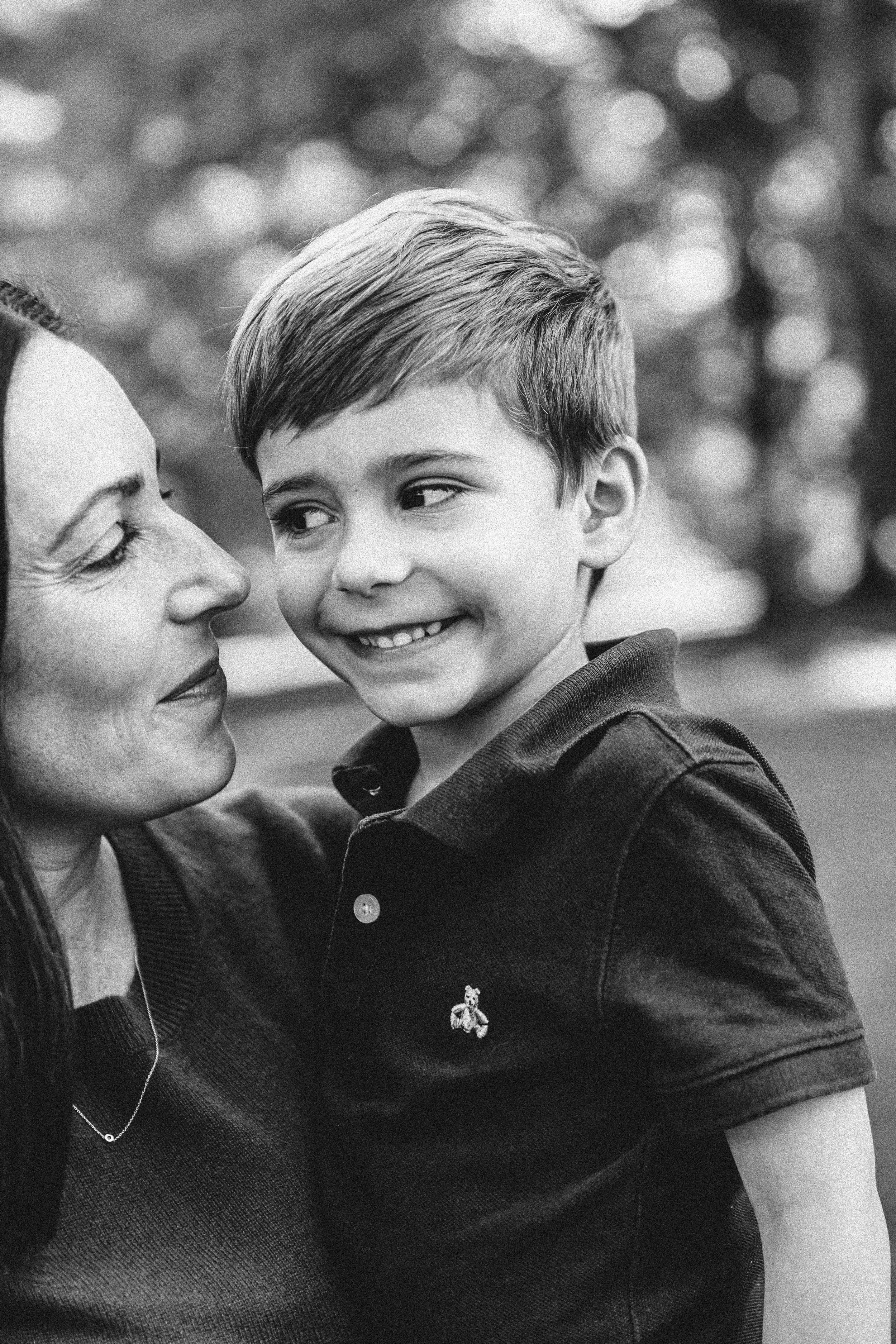 A black and white photo of a woman and a young boy looking at each other and smiling.