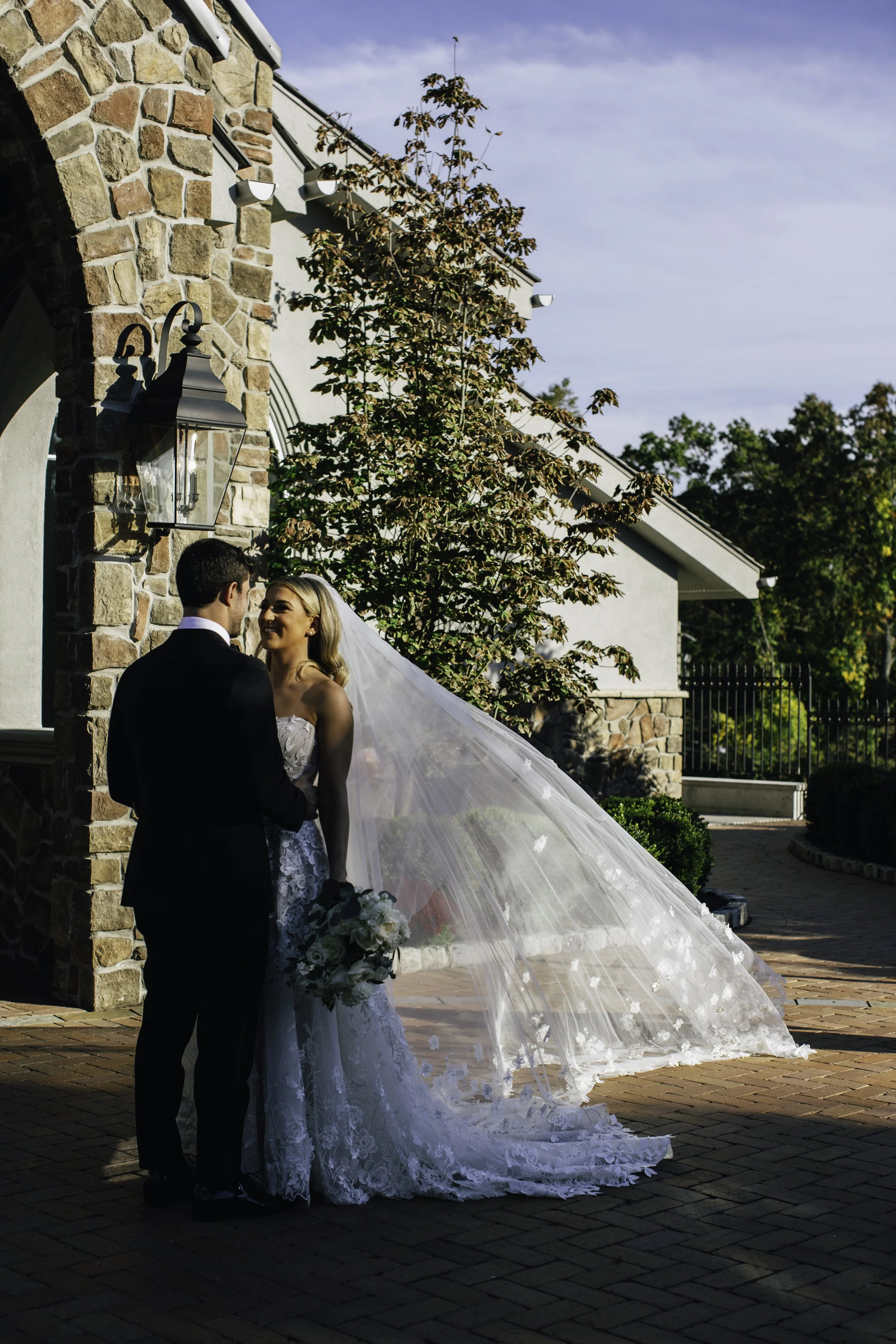 A bride and groom stand facing each other outside a stone building, New York City wedding photographer