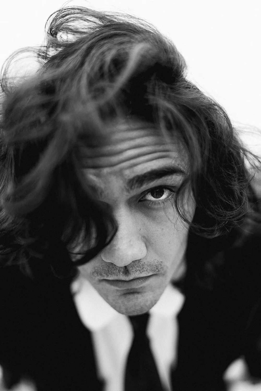 A black and white close-up portrait of a man with long, wavy hair looking into the camera.