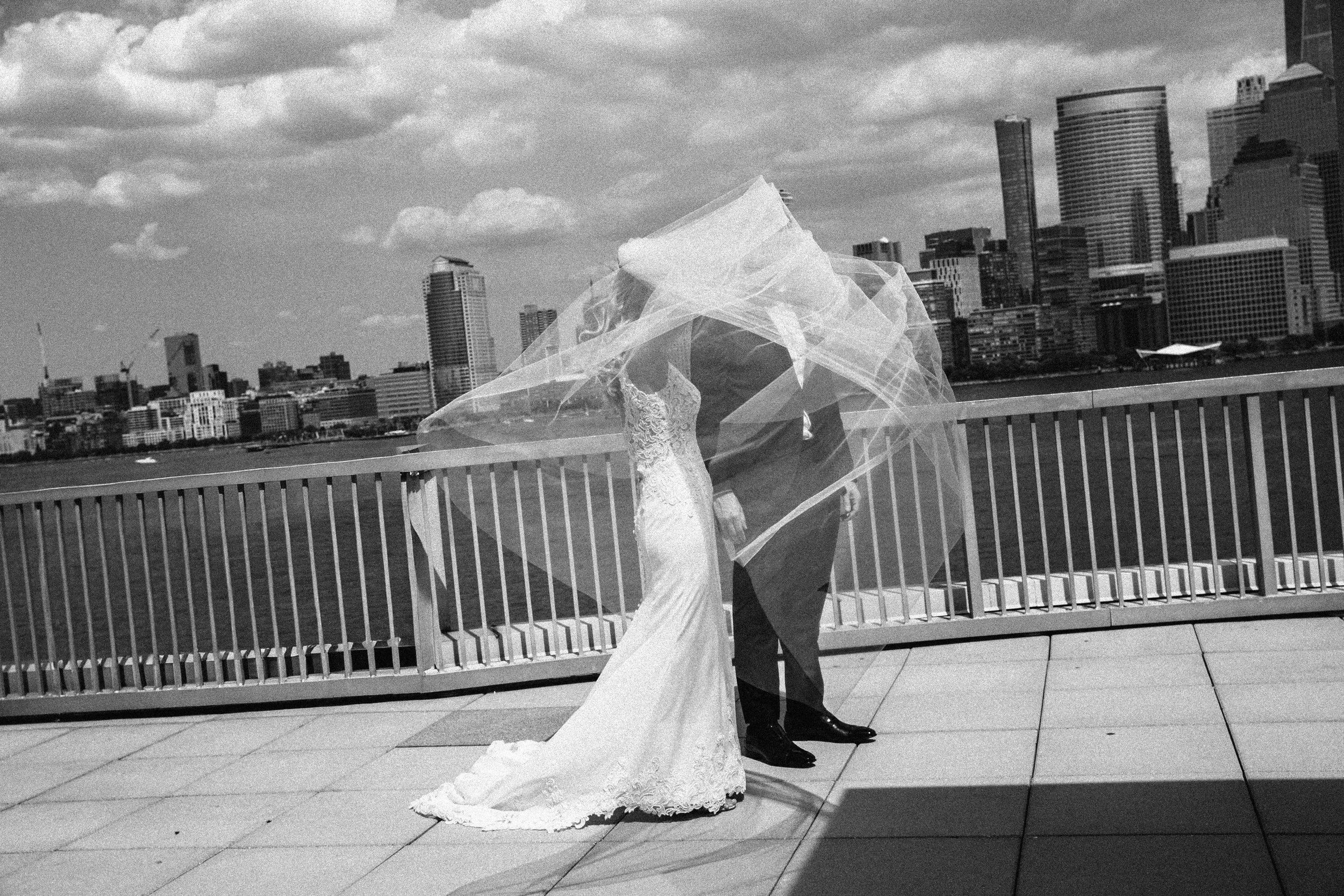 Black and white photo of a bride and groom standing on a rooftop with a city skyline in the background. Documentary wedding photography in NYC