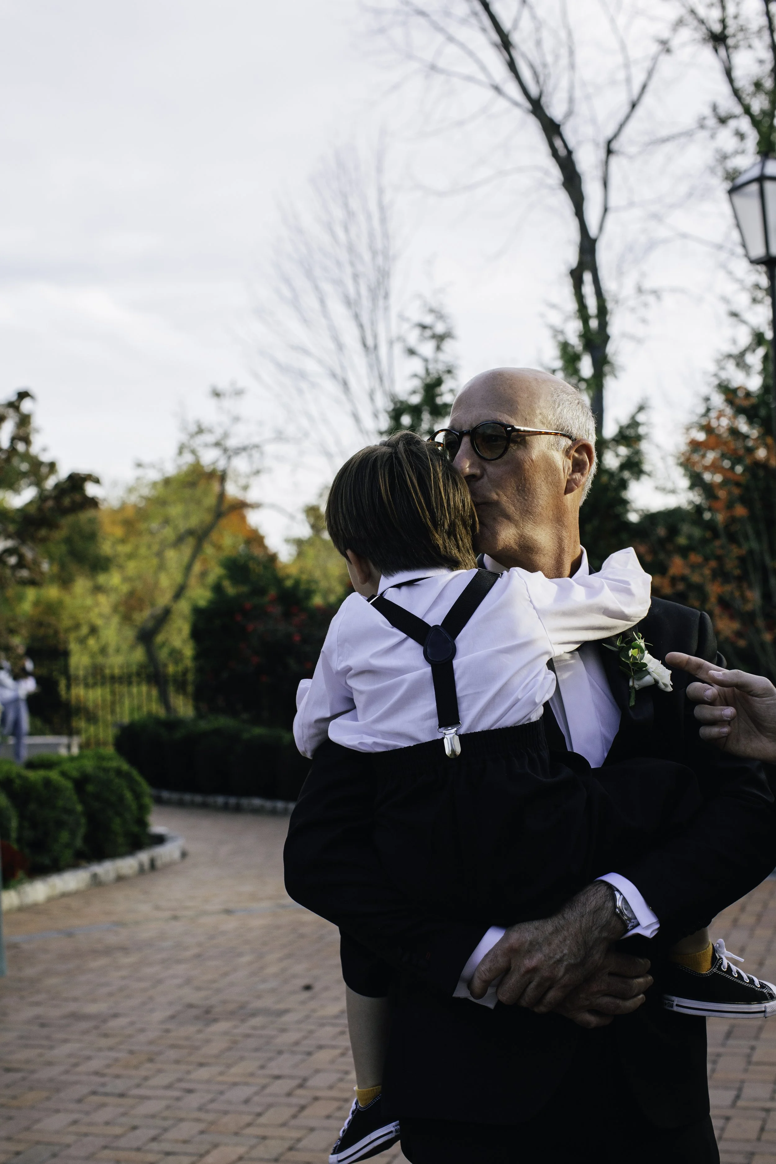 An older man in a suit and glasses holding a young boy in a white shirt and suspenders, NYC wedding photography