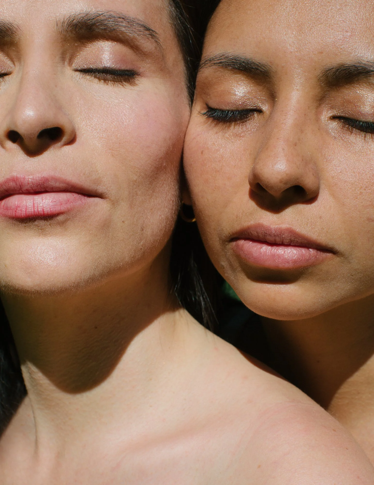Close-up of two women with their eyes closed, facing each other gently touching cheeks.
