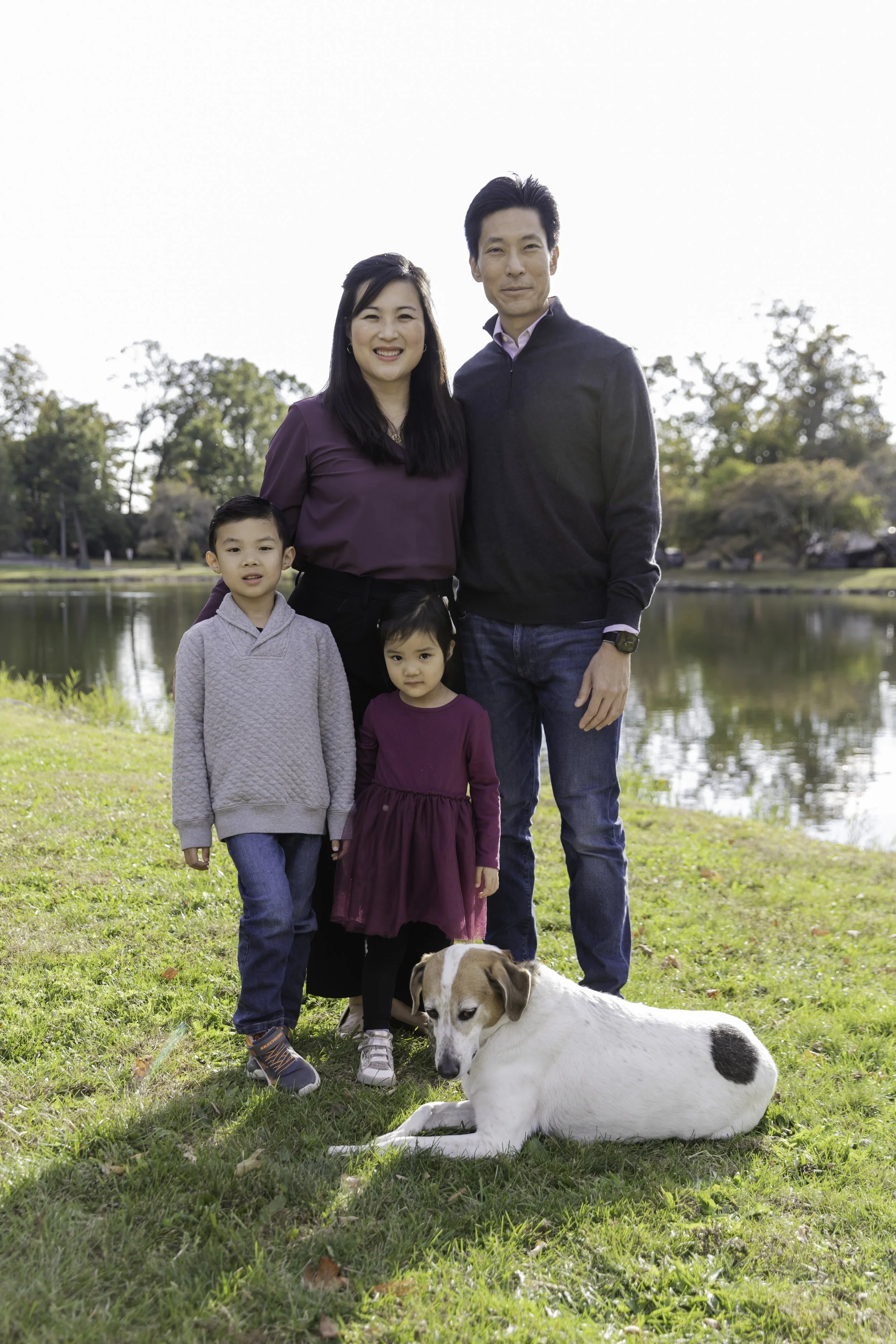 A family of five and a dog with trees and a clear sky in the background. Lifestyle family photography in NYC, natural portrait of family outdoors