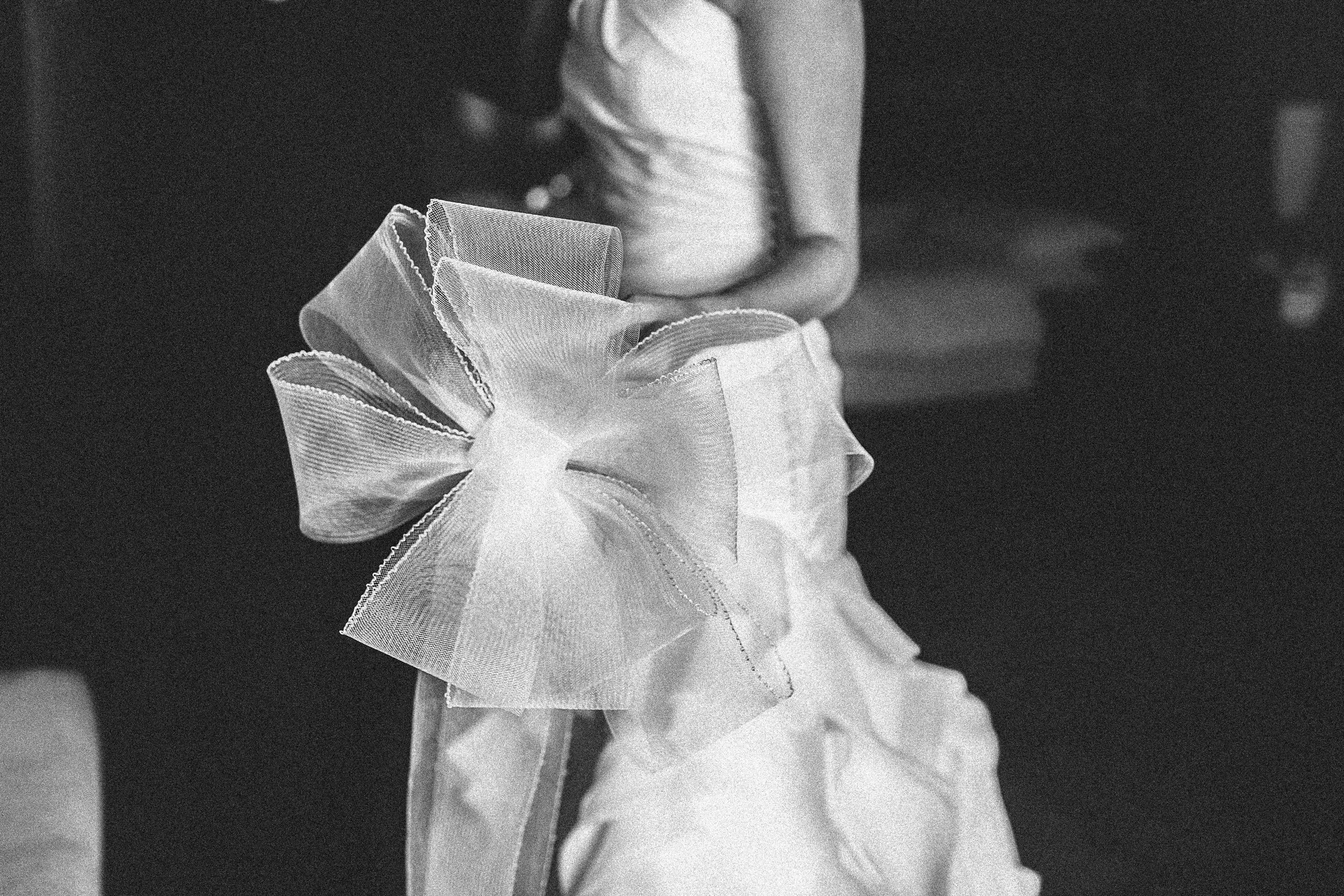 Close-up of a decorative bow made of sheer fabric on a white, ruffled dress or garment.
