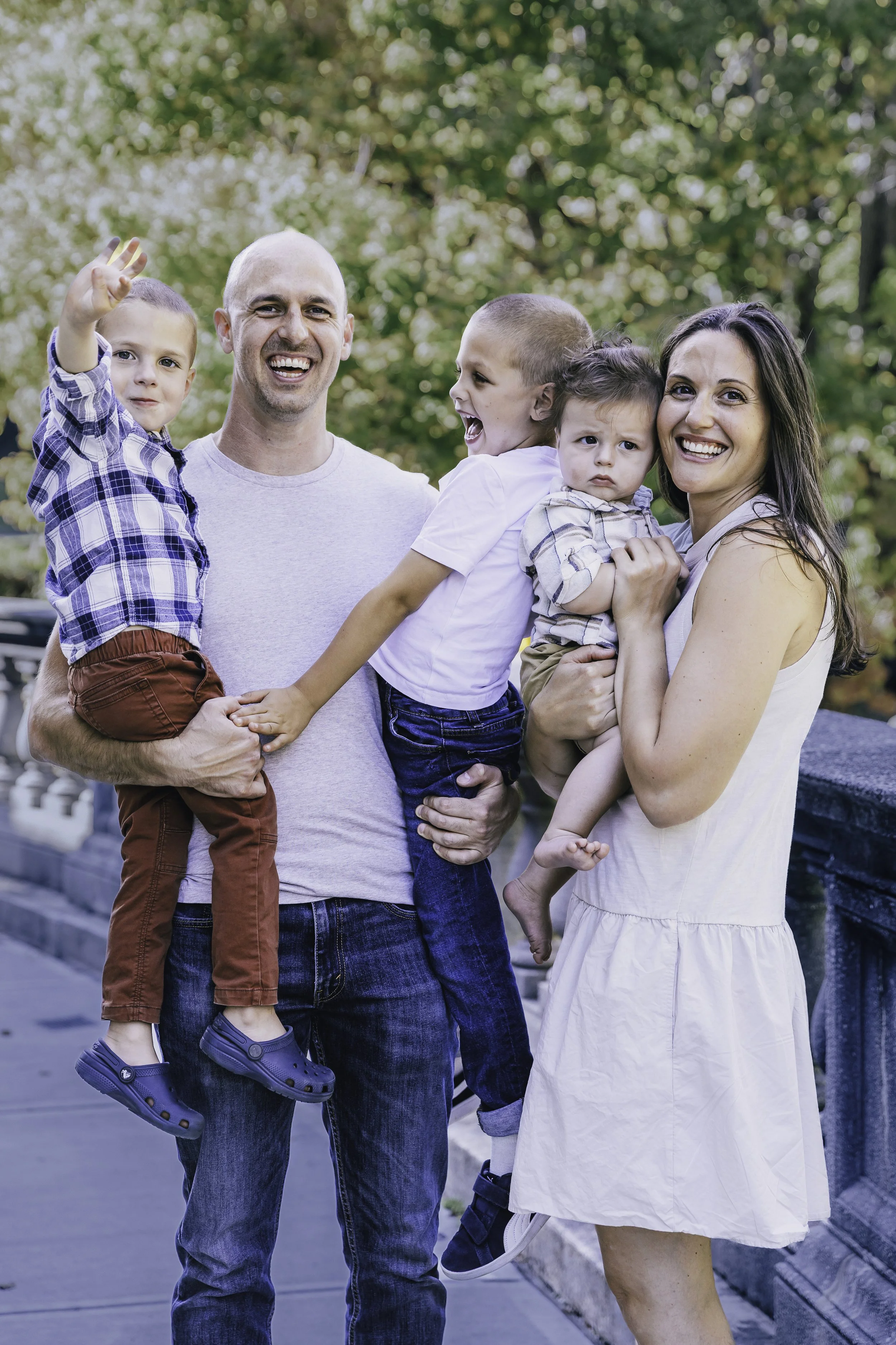 Family of five standing outdoors on a bridge, smiling and playing together. Documentary family photographer in New York City 