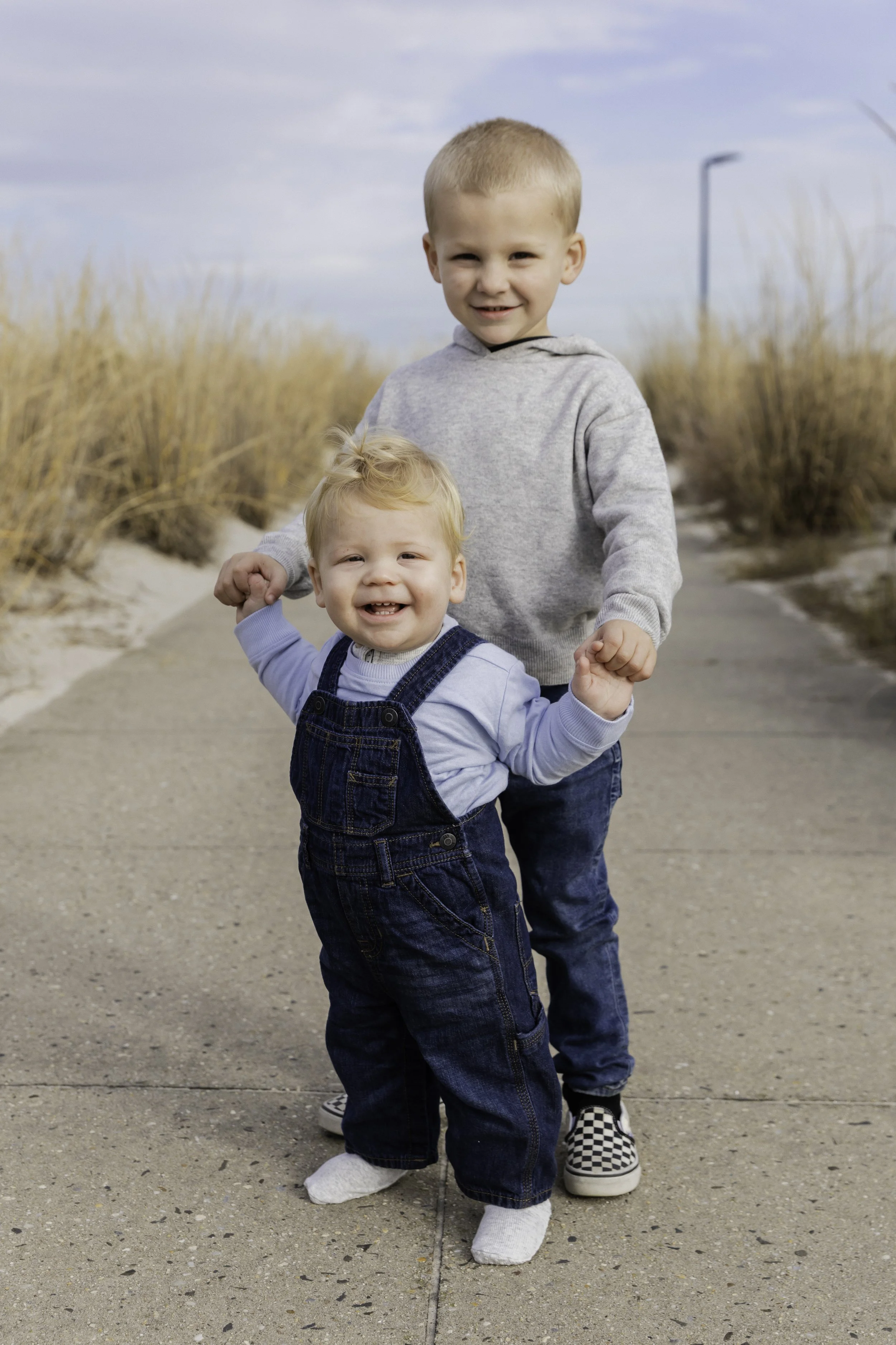 Two young boys smiling on path with tall grass — NYC family photography