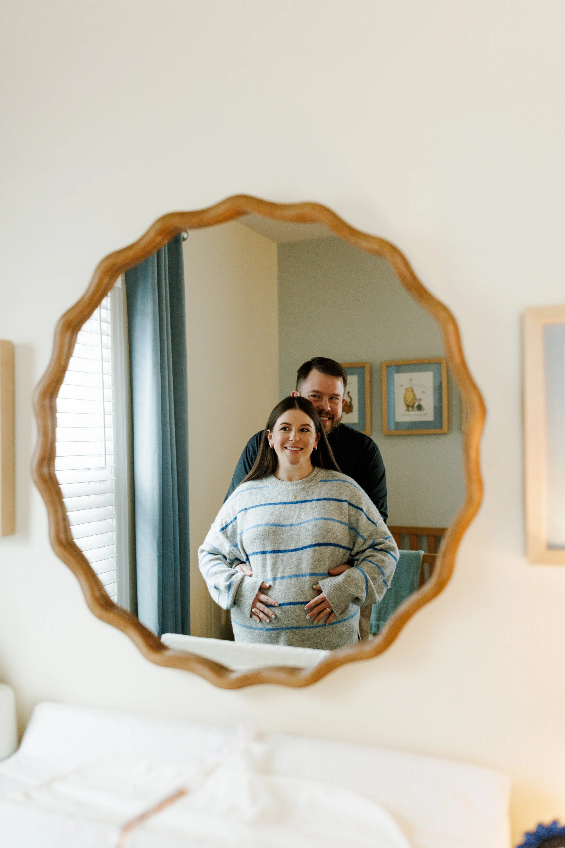 A couple’s reflection in a decorative wall mirror, smiling at each other in a cozy, well-lit room with blue curtains and artwork.