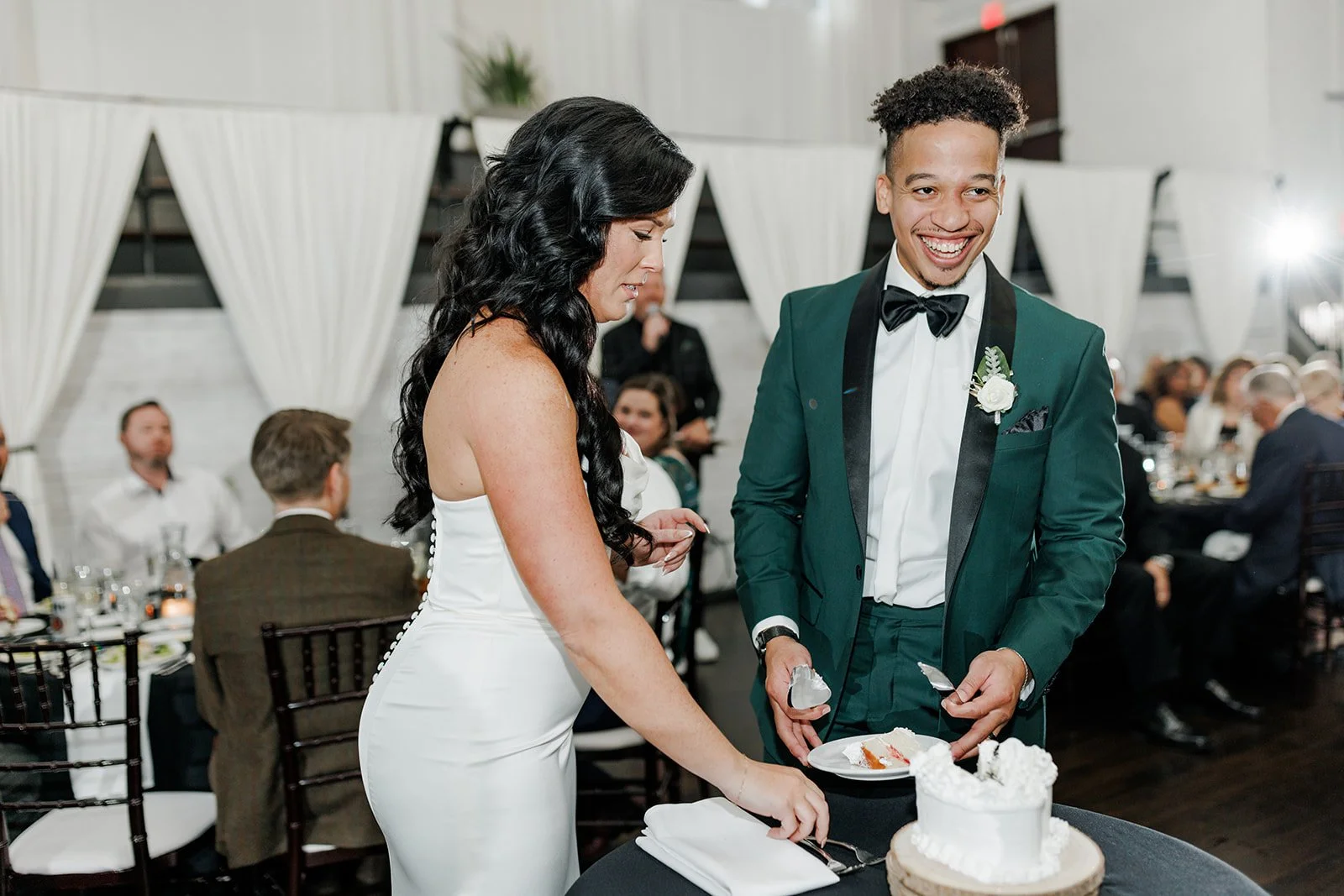 A wedding reception with a bride and groom cutting a wedding cake surrounded by seated guests.