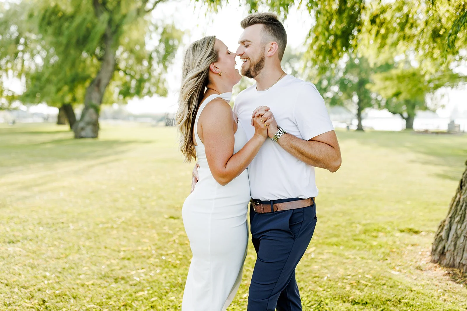 A couple dancing outdoors in a park with green grass and trees, smiling and holding hands.