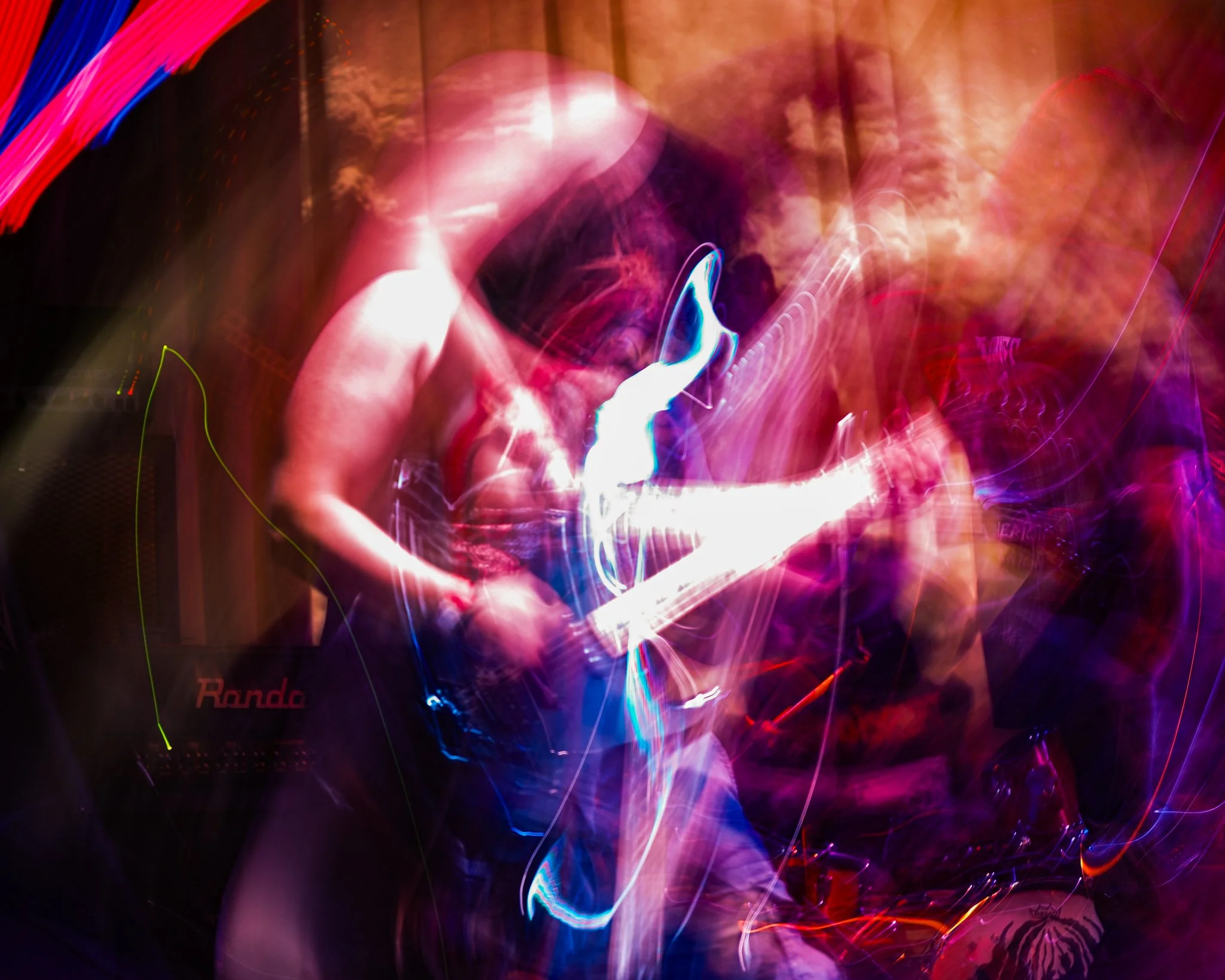 A person playing an electric guitar on stage, illuminated by colorful, swirling lights in a long exposure photograph.