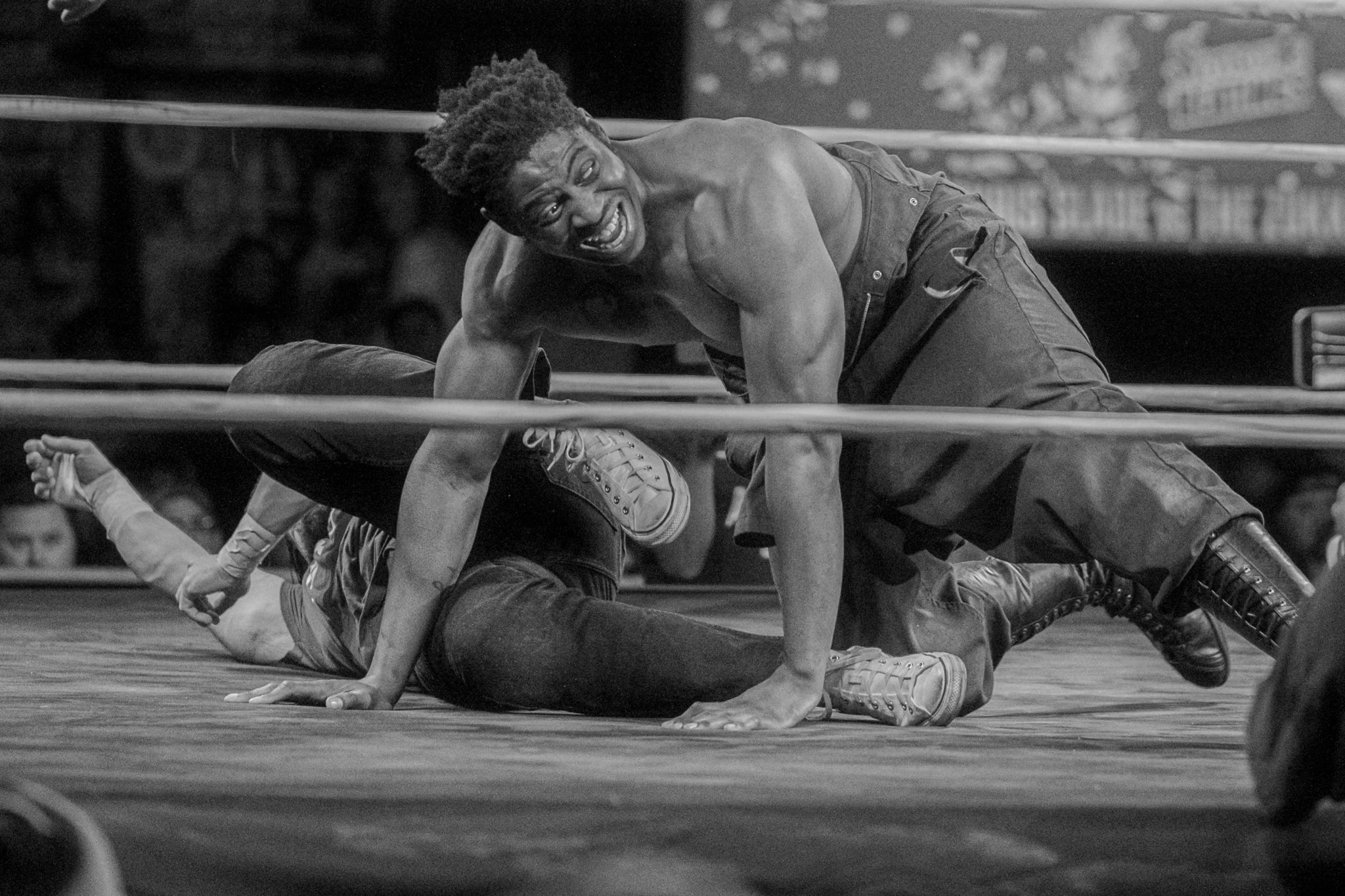 A black and white photo of a wrestling match showing a wrestler on top with a joyous expression, pinning an opponent on the mat.