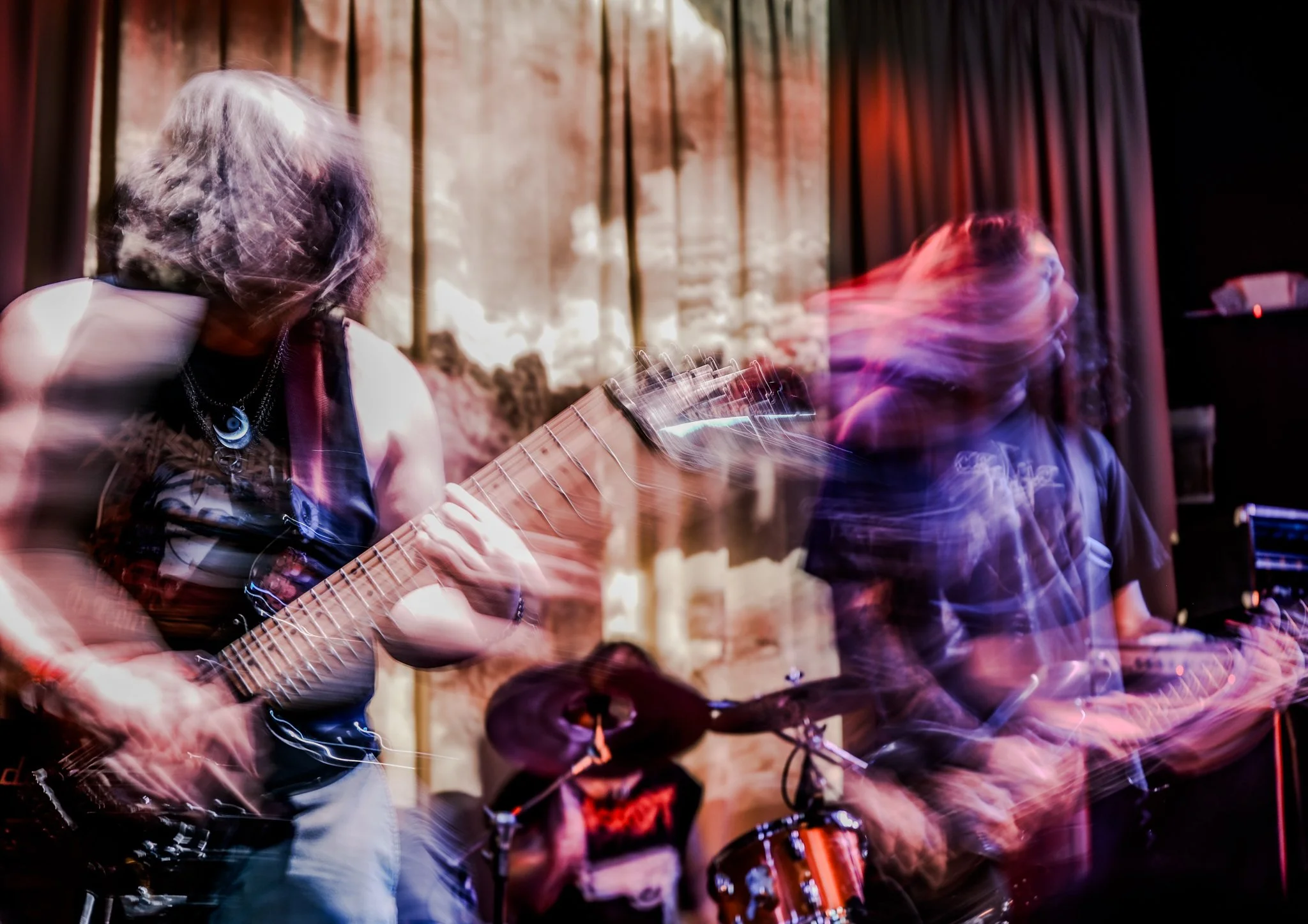Musicians performing with blurred motion effects during a live music session, featuring a guitarist and drummer in a dimly lit setting.