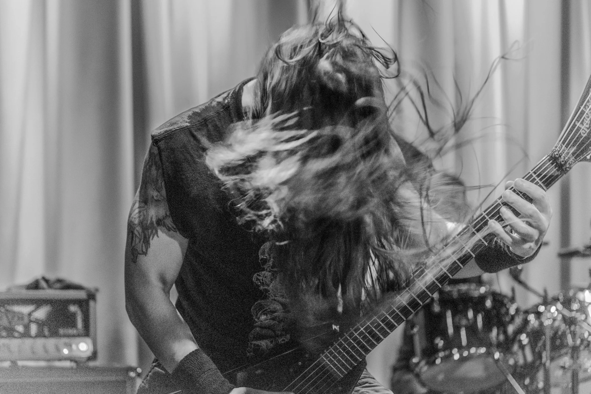 A person with long hair playing an electric guitar on stage, hair flying, in a black-and-white photo