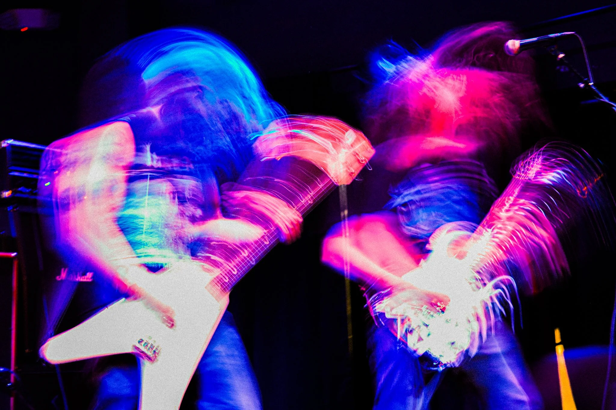 Two guitarists performing on stage with colorful, blurred lights, creating a vibrant, energetic atmosphere.