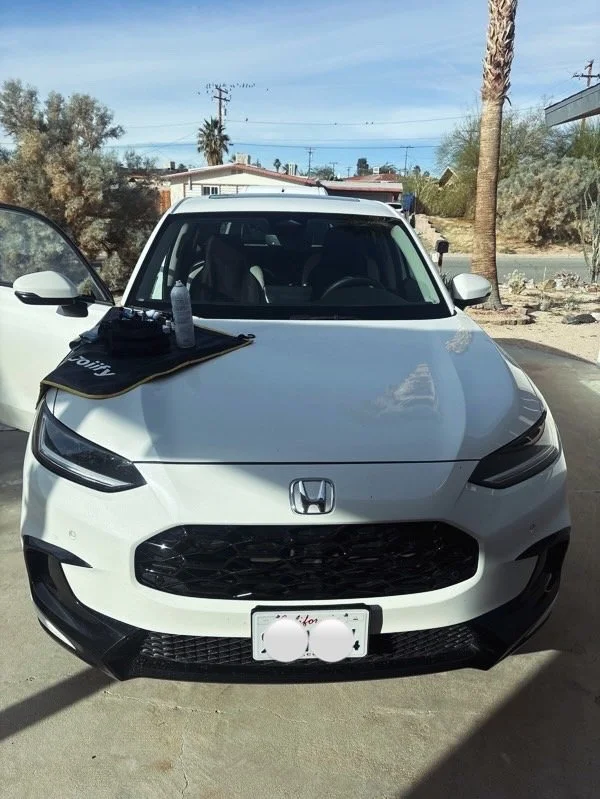 White Honda car parked outside with a cloth and bottle on the hood.