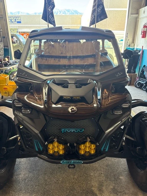 Front view of a black off-road utility vehicle with yellow lights, blue accents, and a large windshield, displayed indoors.