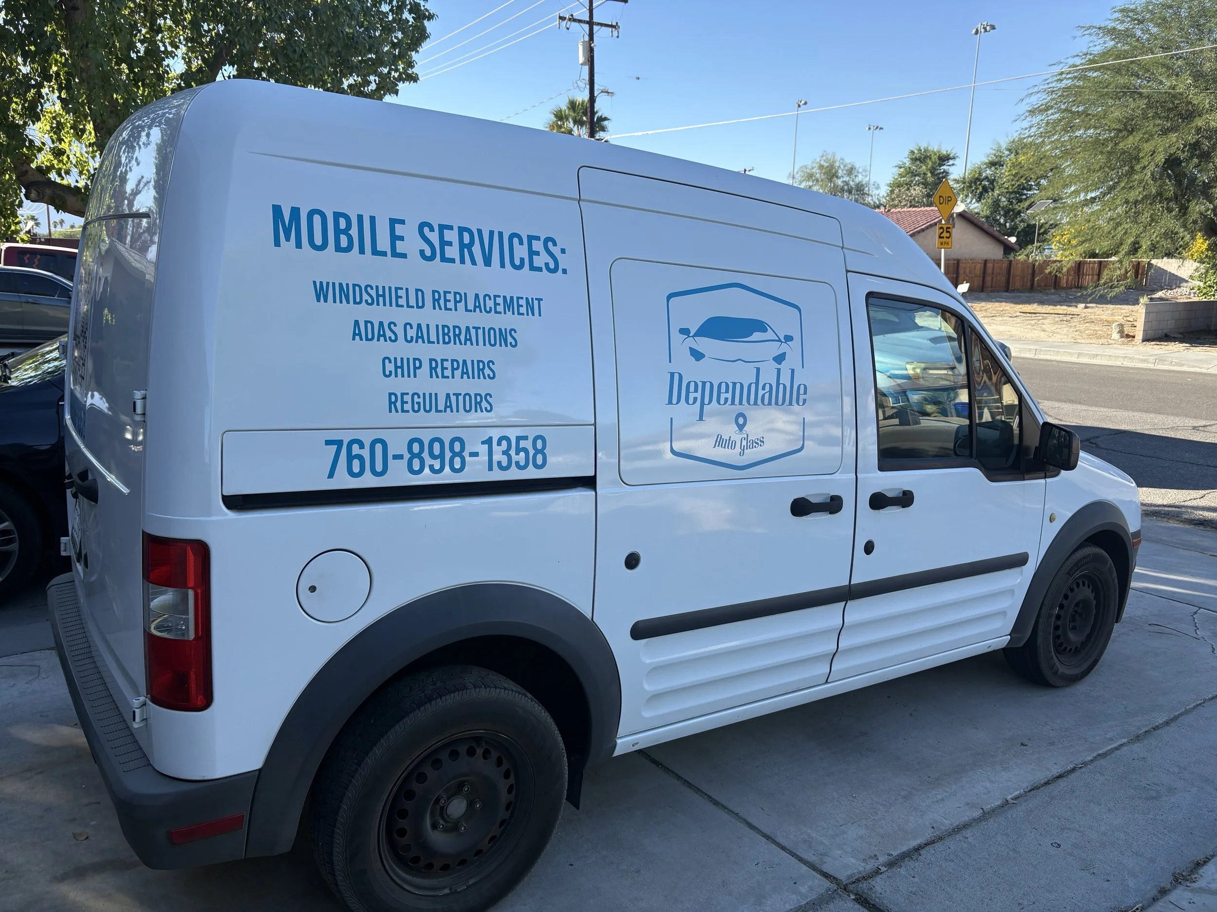 White service van with blue lettering for Dependable Auto Glass, listing services such as windshield replacement, ADAS calibrations, chip repairs, and regulators, with a contact number.