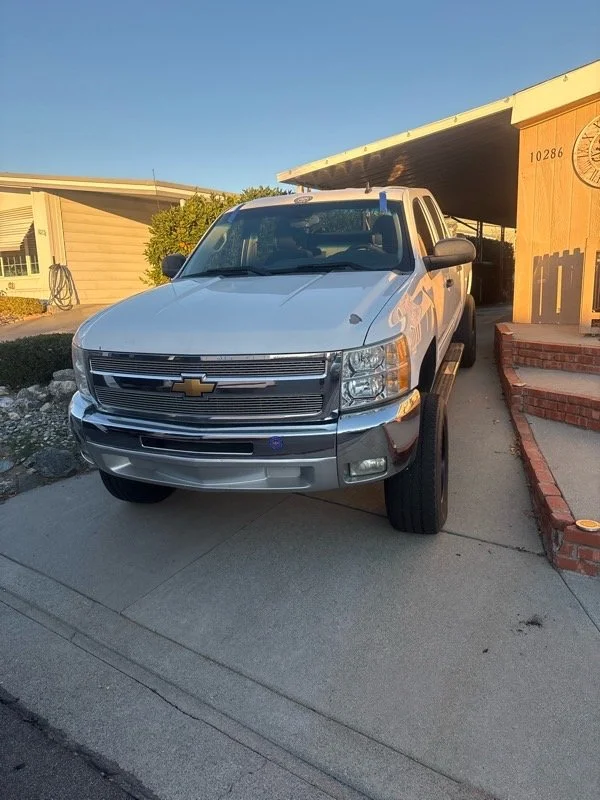 White Chevrolet pickup truck parked on a driveway in front of a house with a small porch and brick steps.