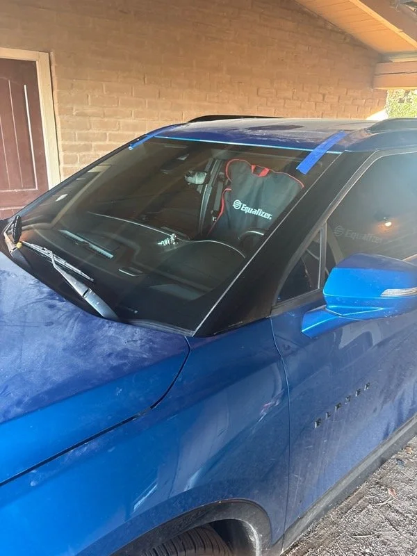 Front passenger side of a blue Chevrolet vehicle parked under a porch, with a racing seat visible inside through the windshield.
