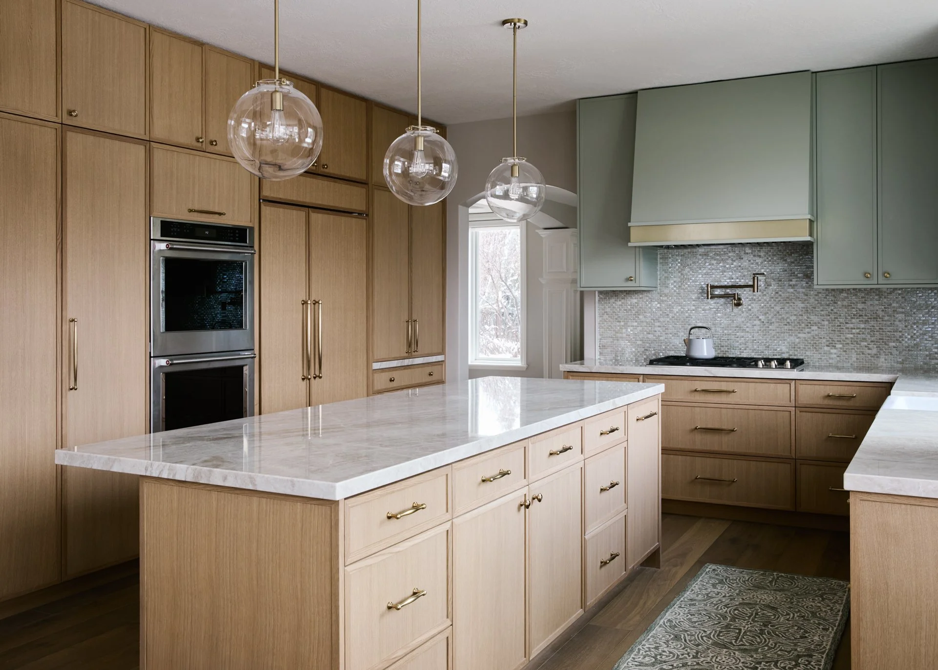 Modern kitchen with wooden cabinets, white marble countertops, a mosaic backsplash, and three hanging glass pendant lights.