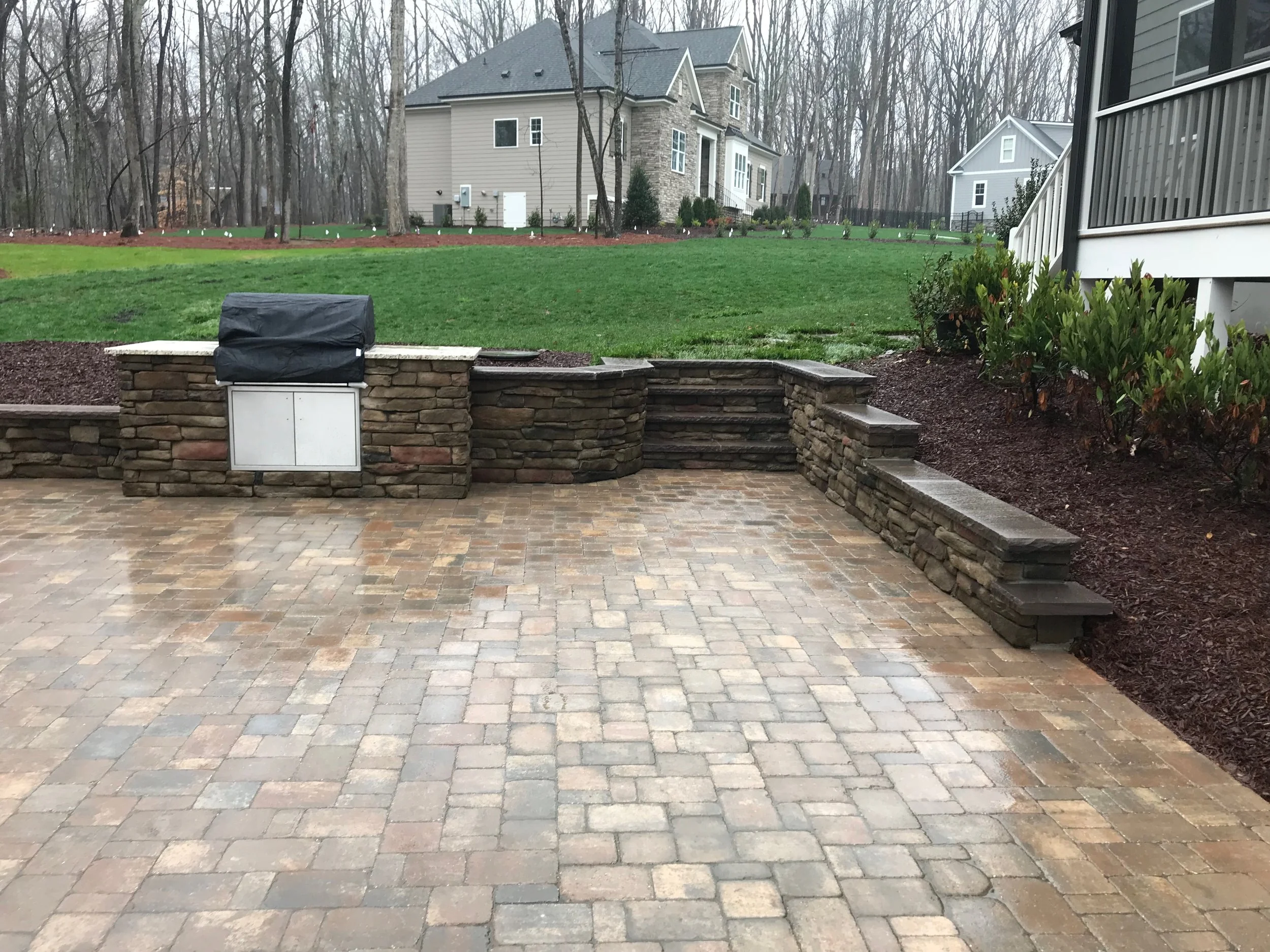 spacious paver patio and outdoor kitchen with retaining walls