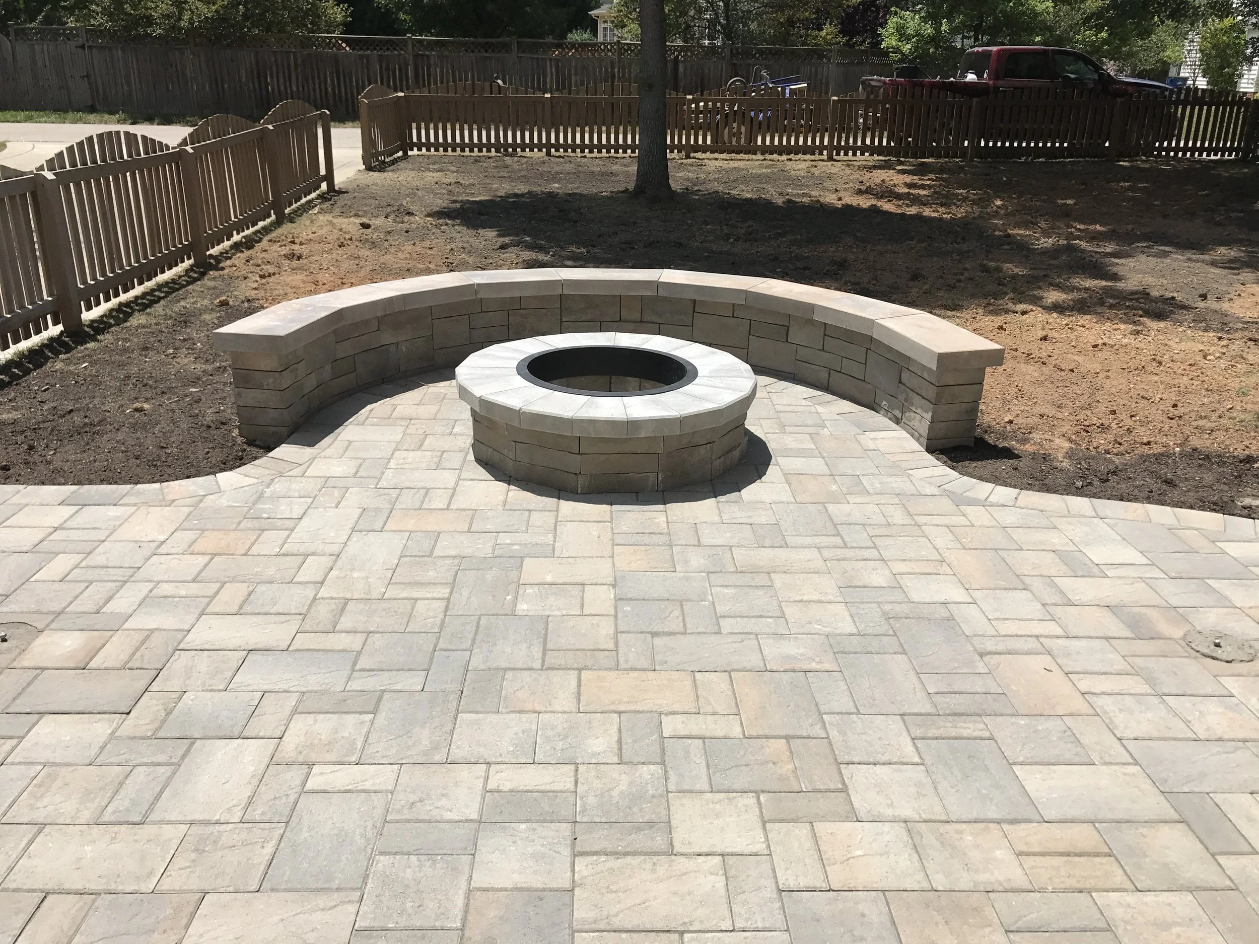 A circular stone fire pit with a surrounding curved stone bench on a paved patio area.