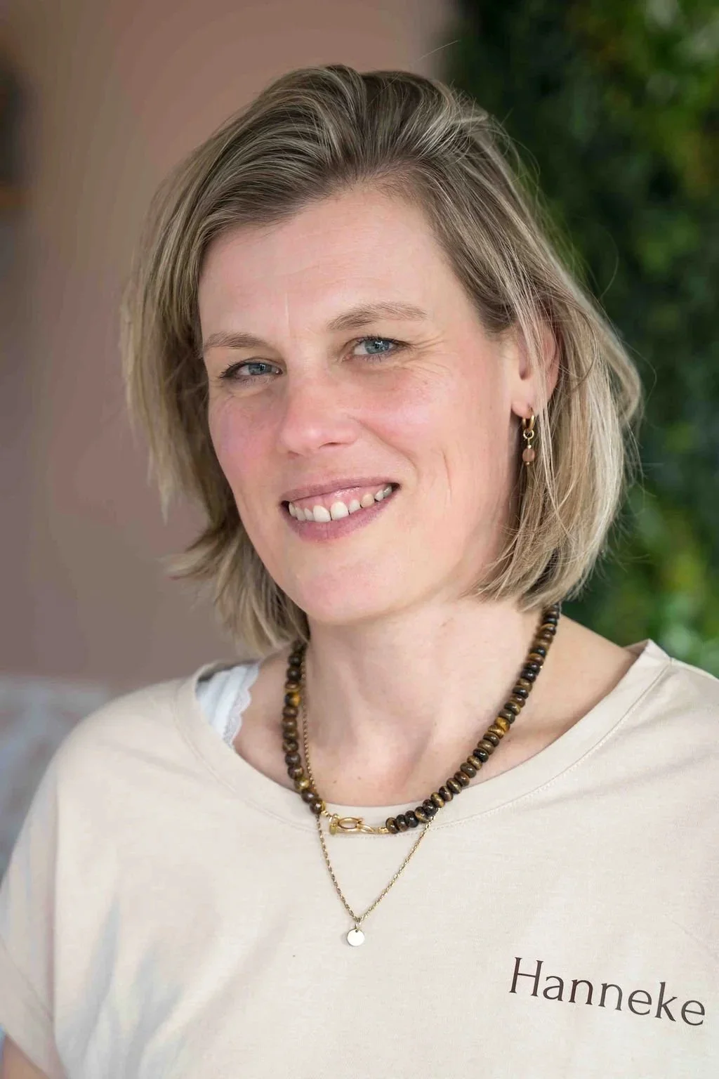 Portret van een vrouw met blond haar, zittend voor een haardvuur, in een huis met boekenplank op de achtergrond.