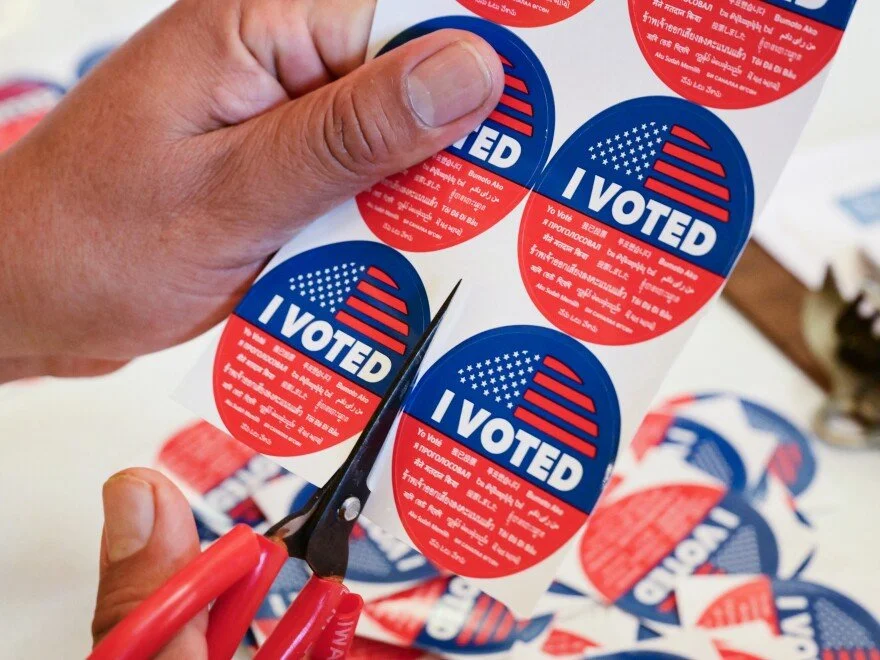 Person cutting out American-themed 'I Voted' stickers with scissors.