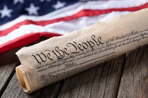 A scroll of the U.S. Constitution on a wooden surface, with part of the American flag in the background.