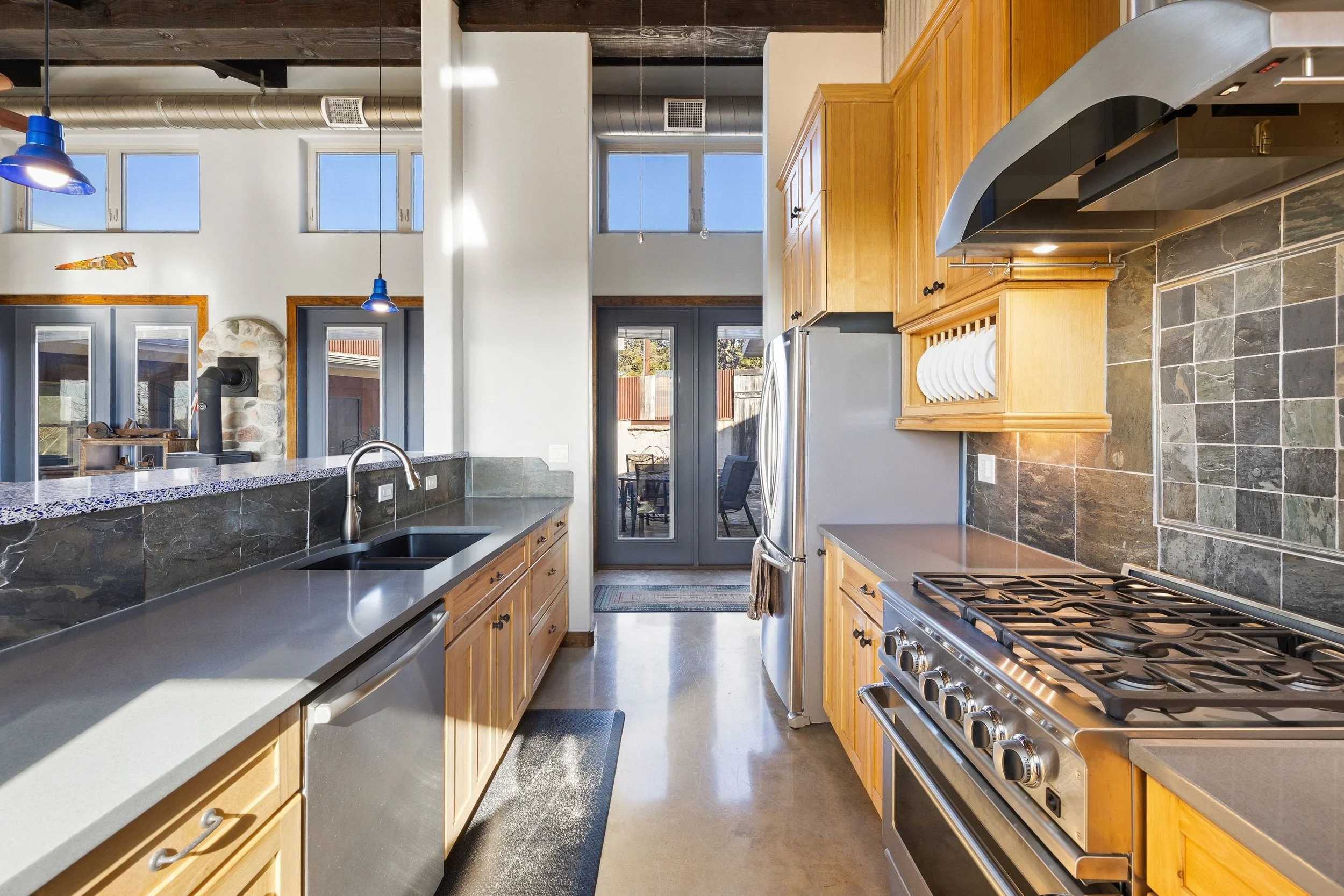 Modern kitchen with wooden cabinets, a stainless steel refrigerator, gas stove, black backsplash tiles, and a large windowed door leading to an outdoor patio.