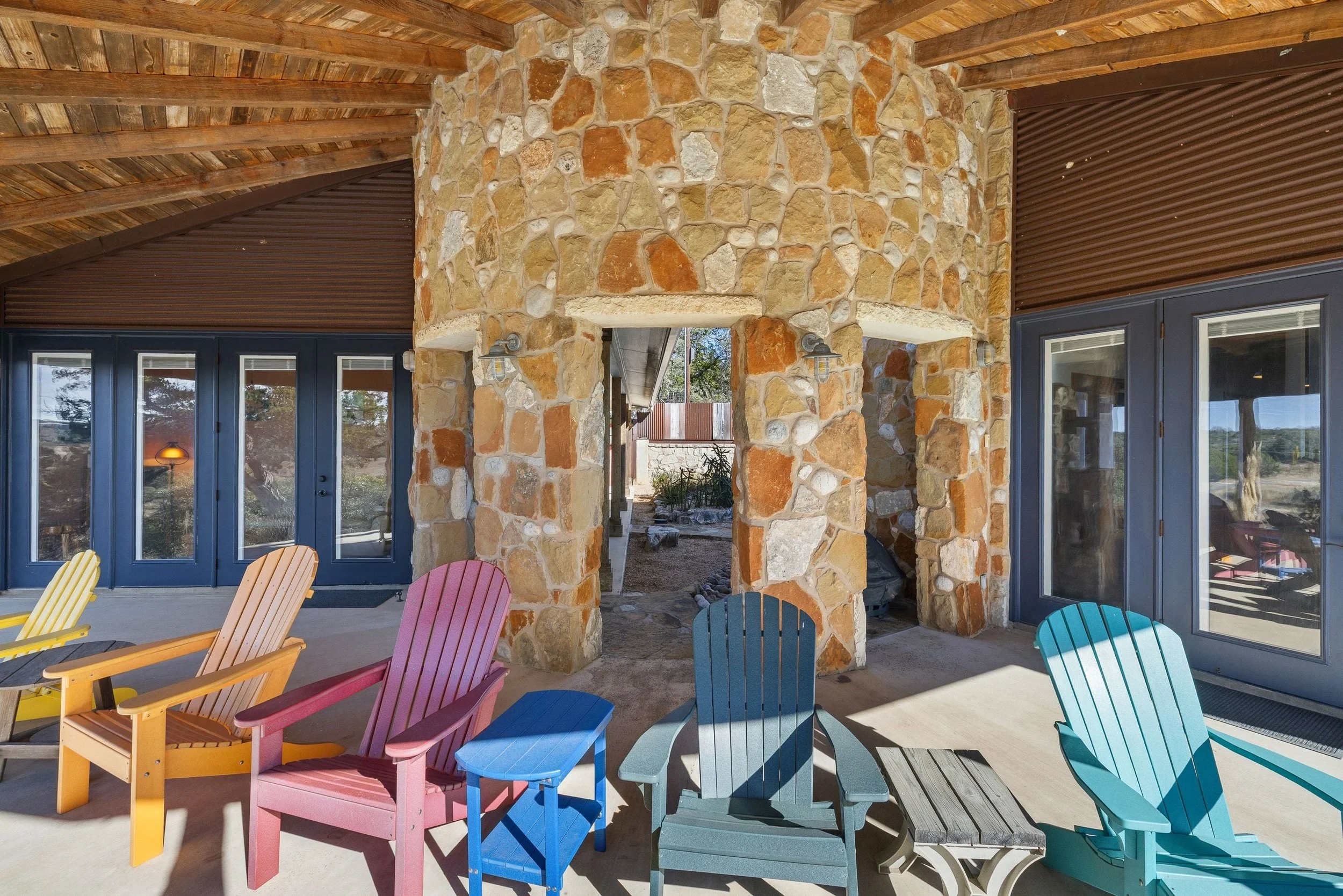 Colorful Adirondack chairs on patio in front of stone and wood building with glass doors and windows