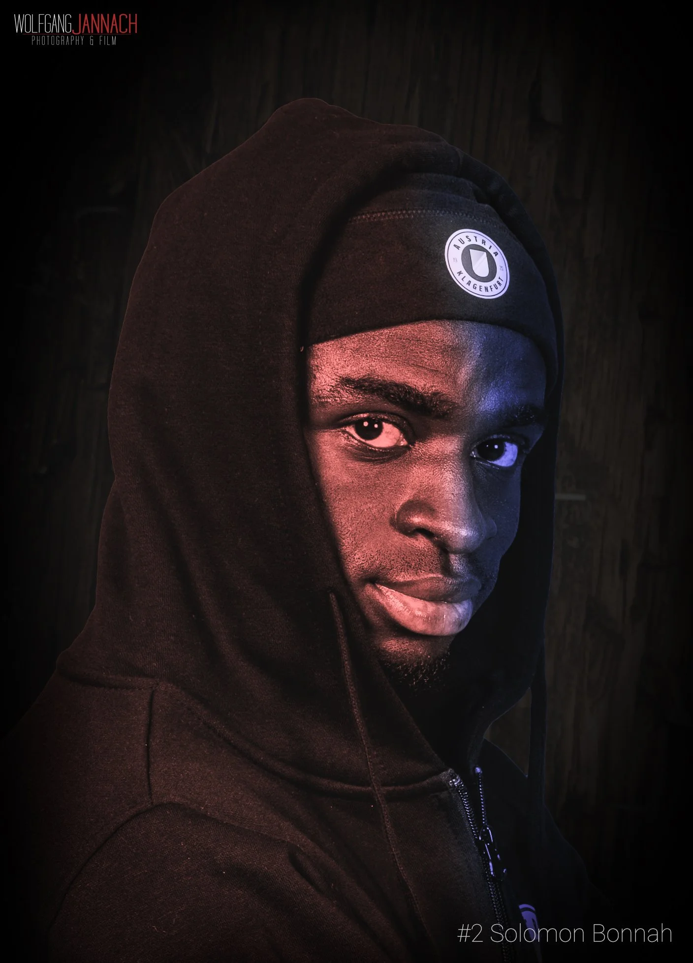 Porträt eines schwarzen Mannes mit schwarzen Hoodie und Mütze, das auf einer dunklen Holzoberfläche steht. Der Mann blickt direkt in die Kamera, halb im Schatten. Text auf dem Bild: "#2 Solomon Bonnah".