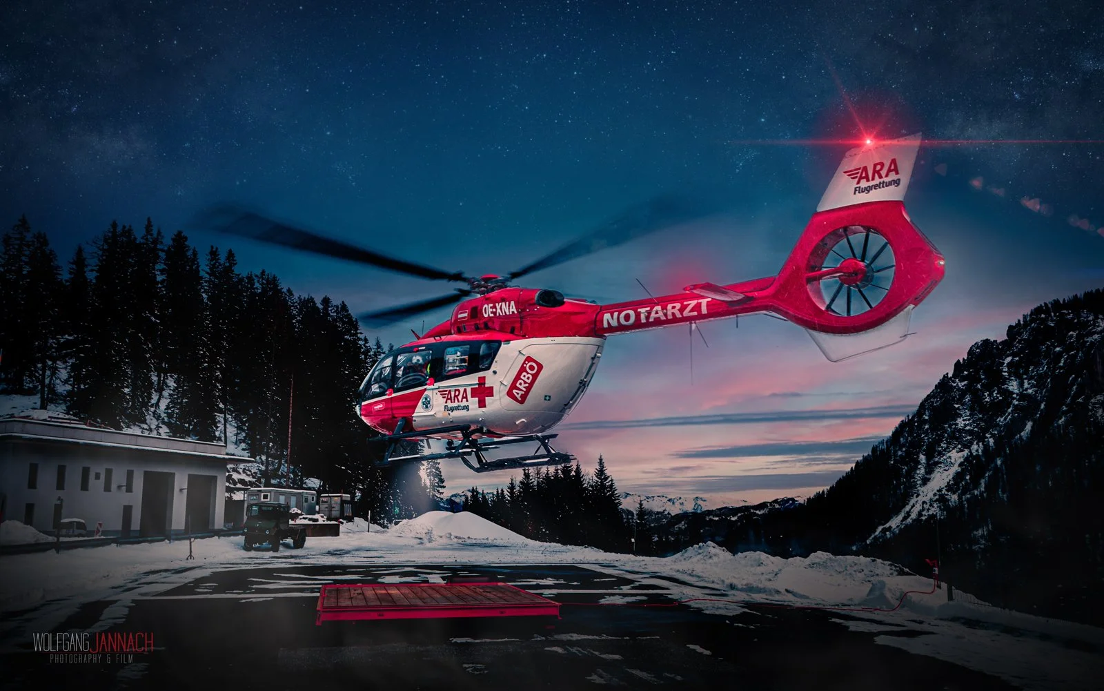 Ein Rettungsheli fliegt nachts über verschneites Berggebiet mit einem Sternenhimmel im Hintergrund.