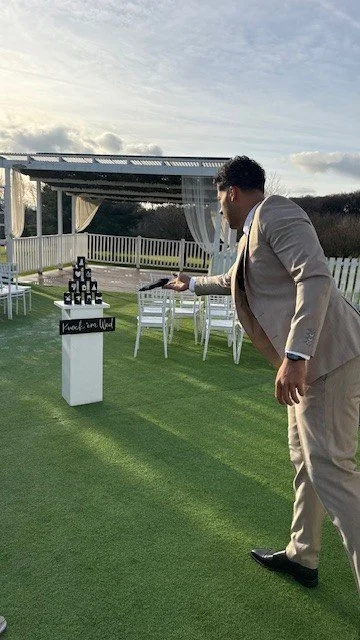 A man in a beige suit playing a ring toss game outside on grass during daytime.