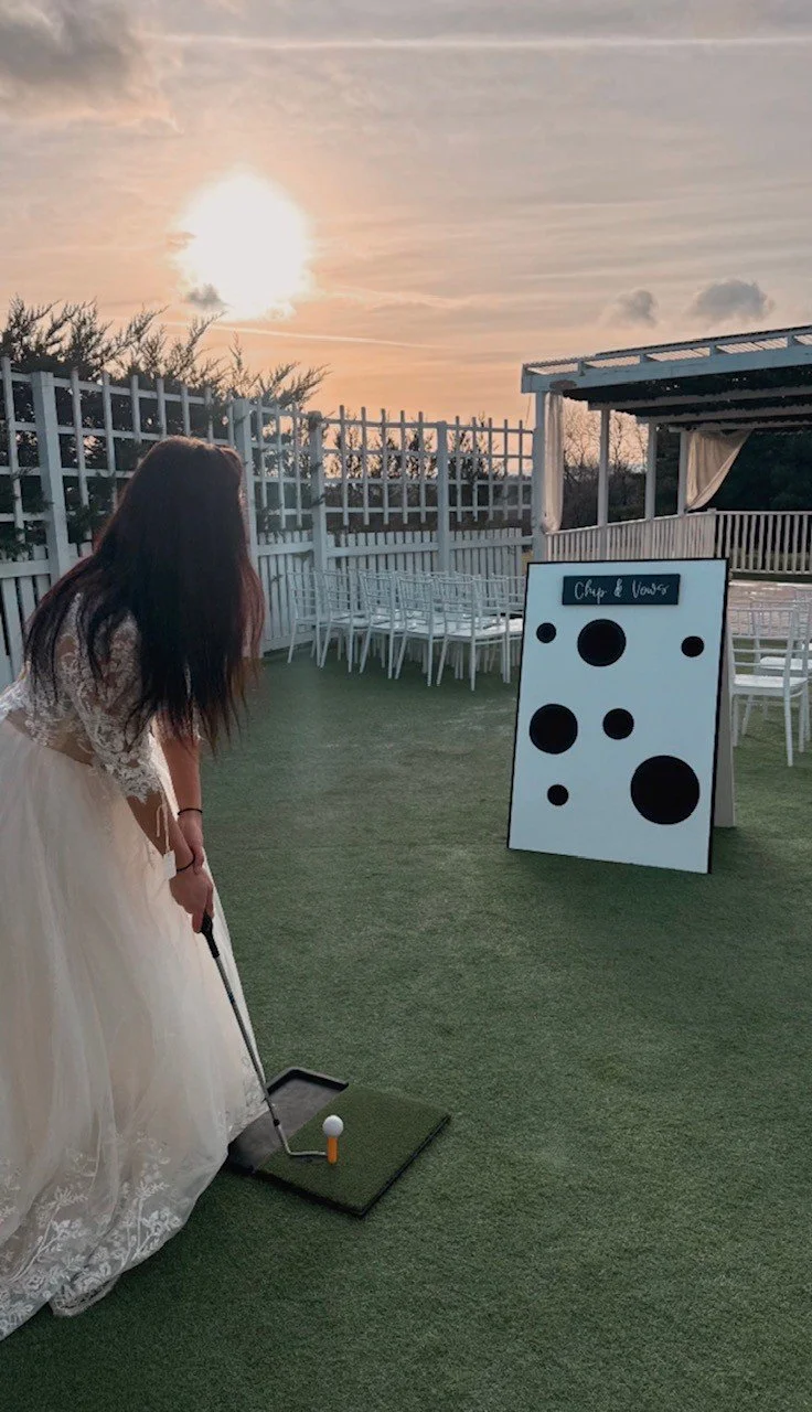 A woman in a wedding dress playing mini golf on an outdoor green at sunset.