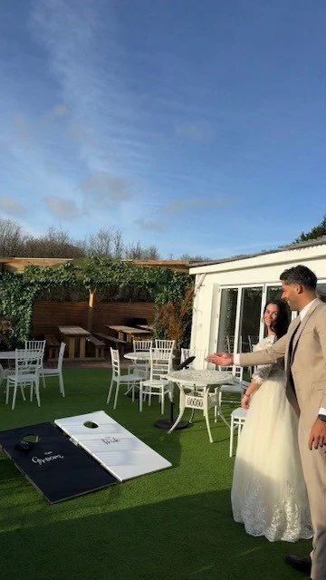 A wedding reception outdoor setting with a couple standing under a tent, with tables and chairs, and a clear blue sky.