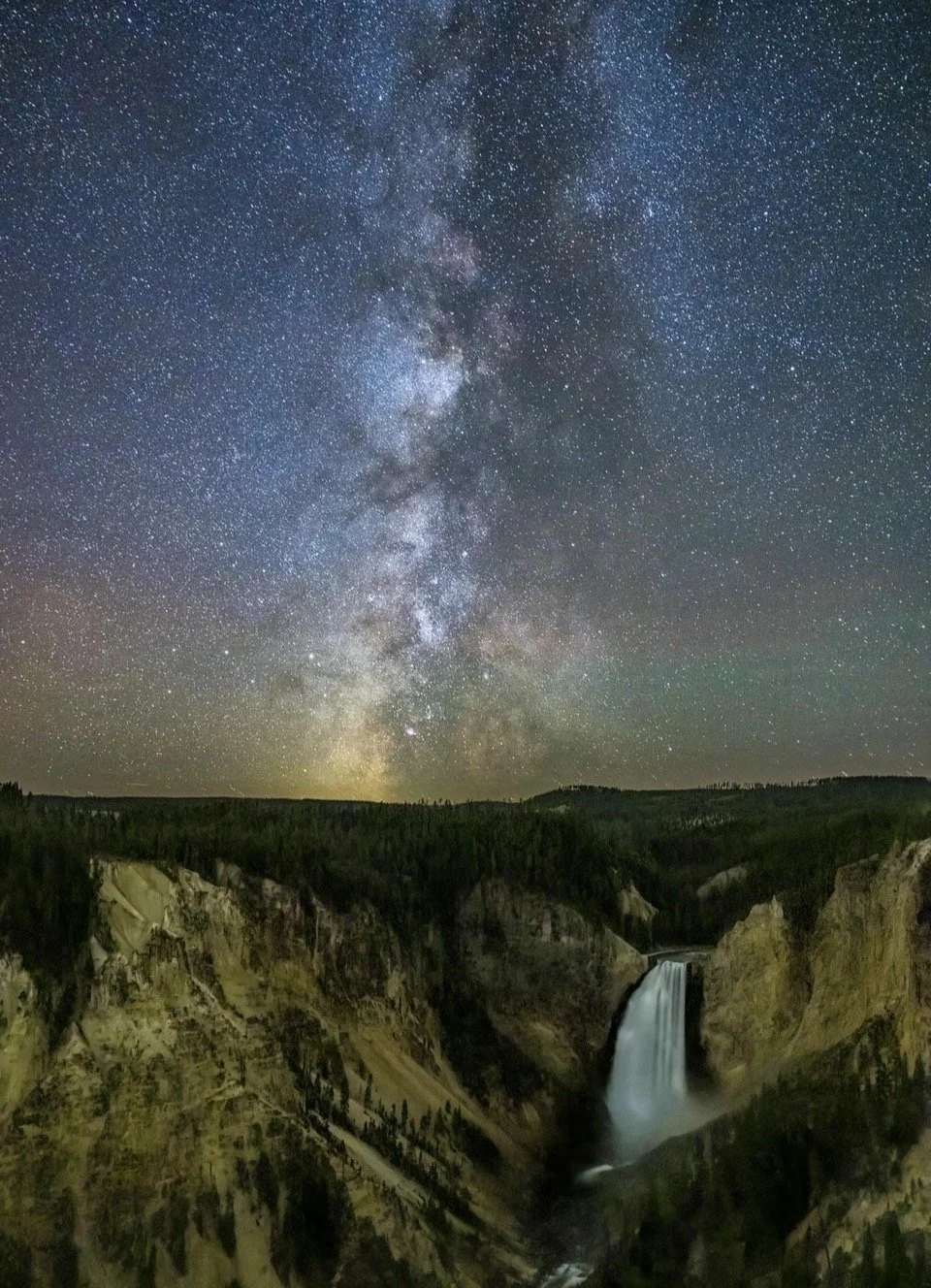 Night sky filled with stars and the Milky Way over a landscape with a waterfall and canyon.