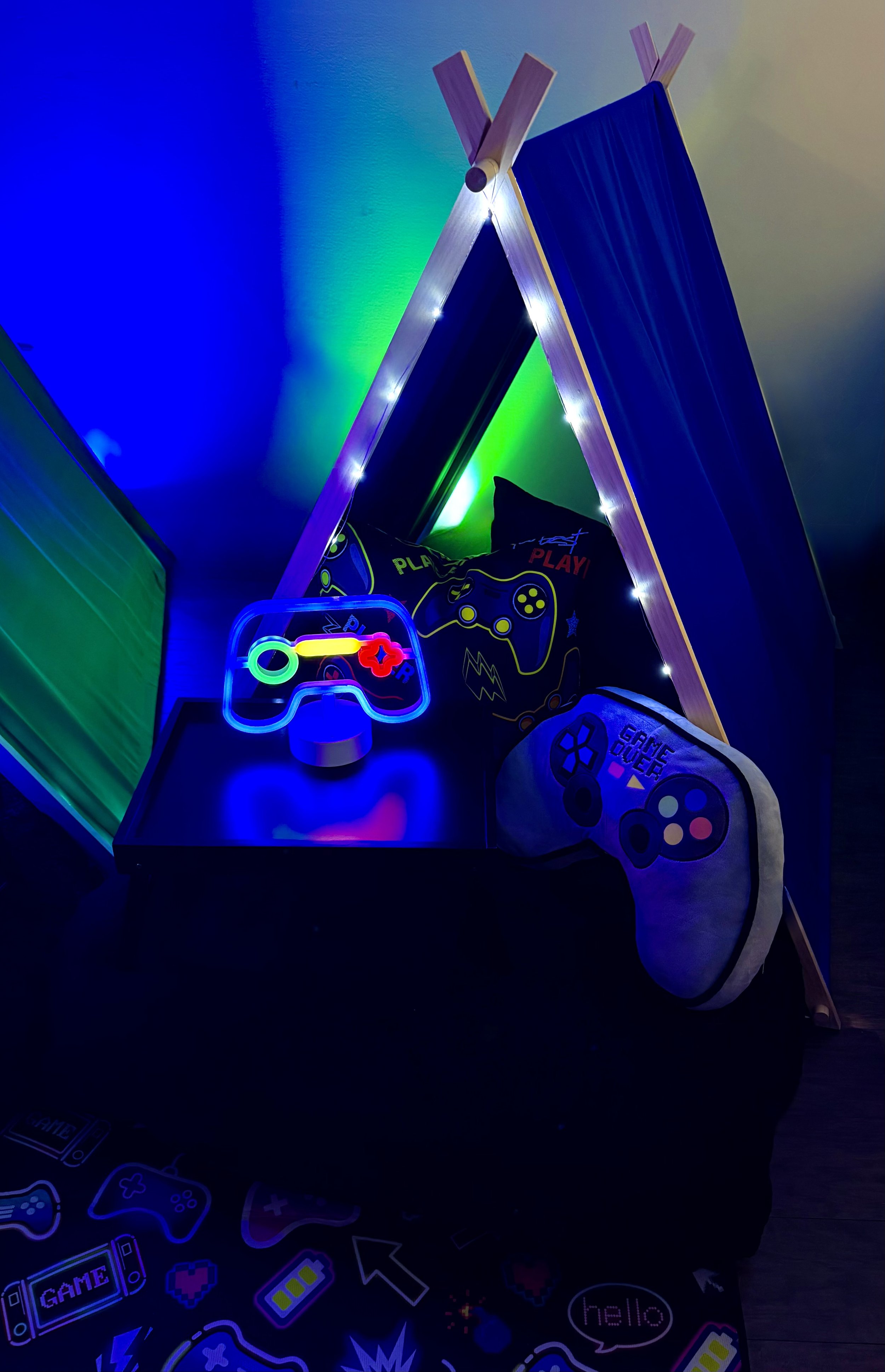 Decorative gaming setup with LED lights, gaming controller lights, gaming-themed pillows, and a small table with gaming stickers.