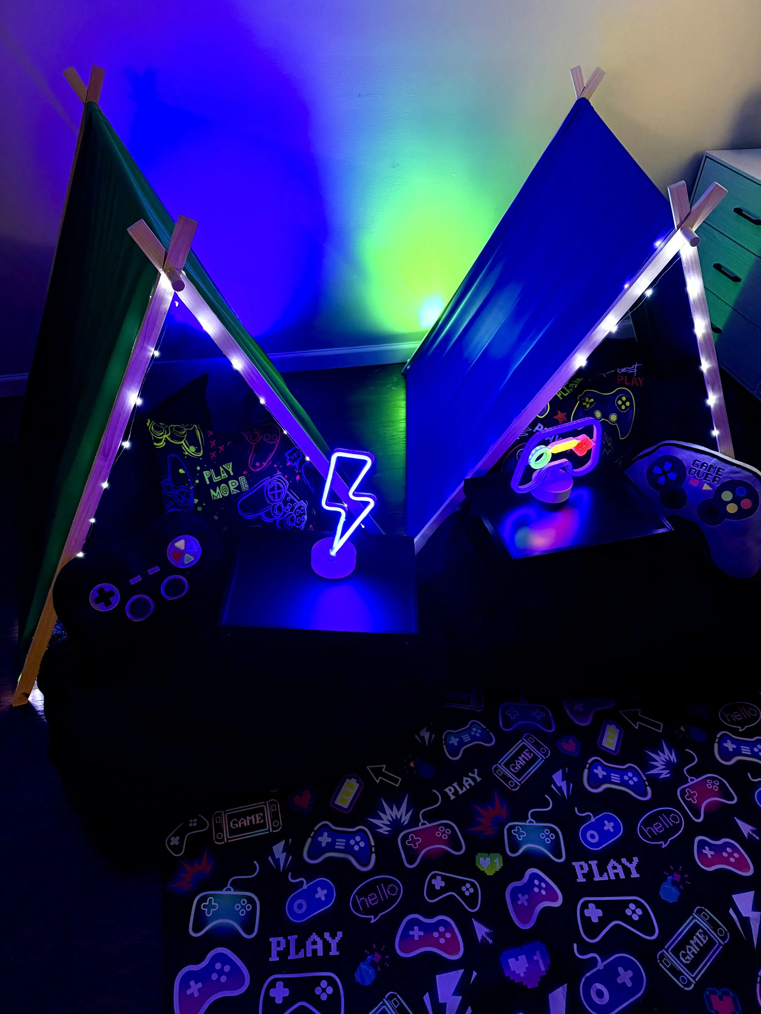 A gaming setup with two small tents, LED lights, and various game-themed decorations, including game controllers and 'PLAY' signs, creating a vibrant, colorful atmosphere.