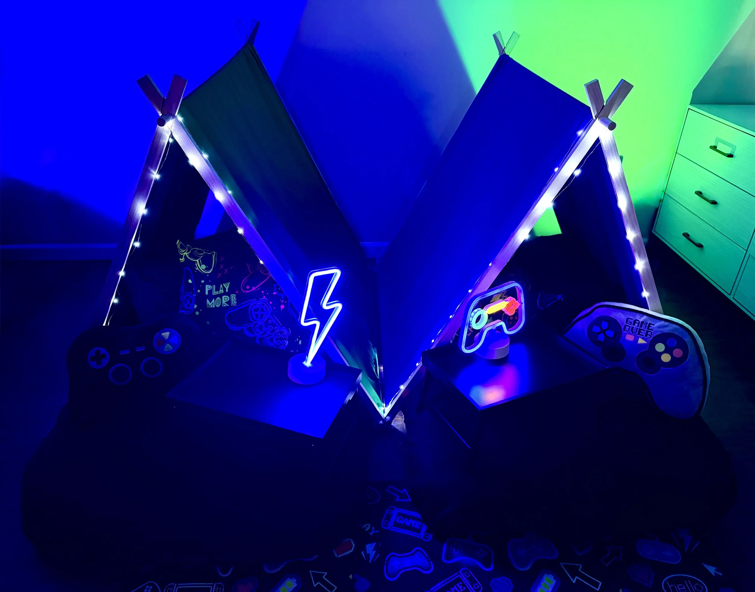 Colorful gaming-themed room with neon signs, gaming controllers, and LED lights in blue, green, and purple hues.
