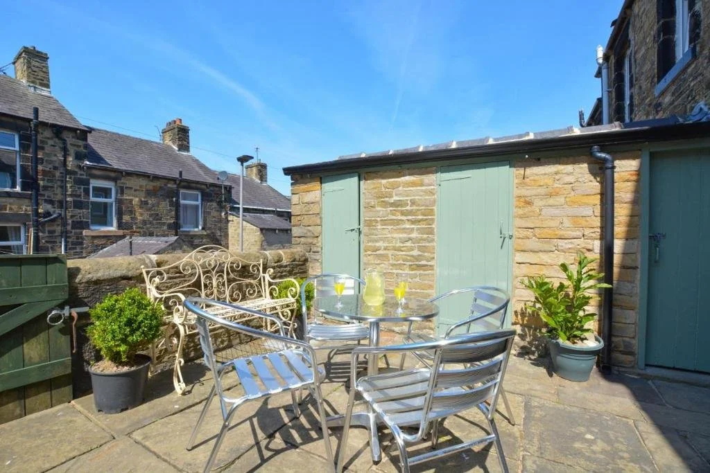 Green Gables courtyard with garden furniture to relax or eat your dinner.  This shows the useful lockable shed and the outside toilet to the right with light green doors.  This is on the edge of the garden and features several plants in pots.