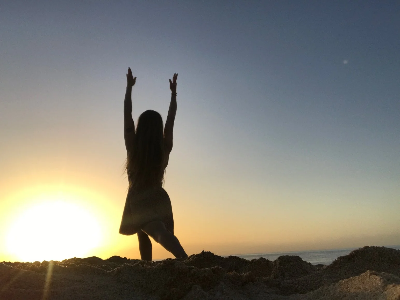 Silhouette of a woman standing on a sandy beach at sunset with arms raised