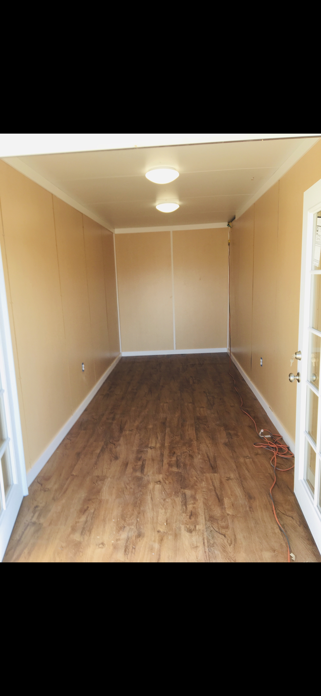 Empty room with wood flooring, beige walls, white trim, and ceiling lights. French door with glass panels on the right, electrical wires on the floor.