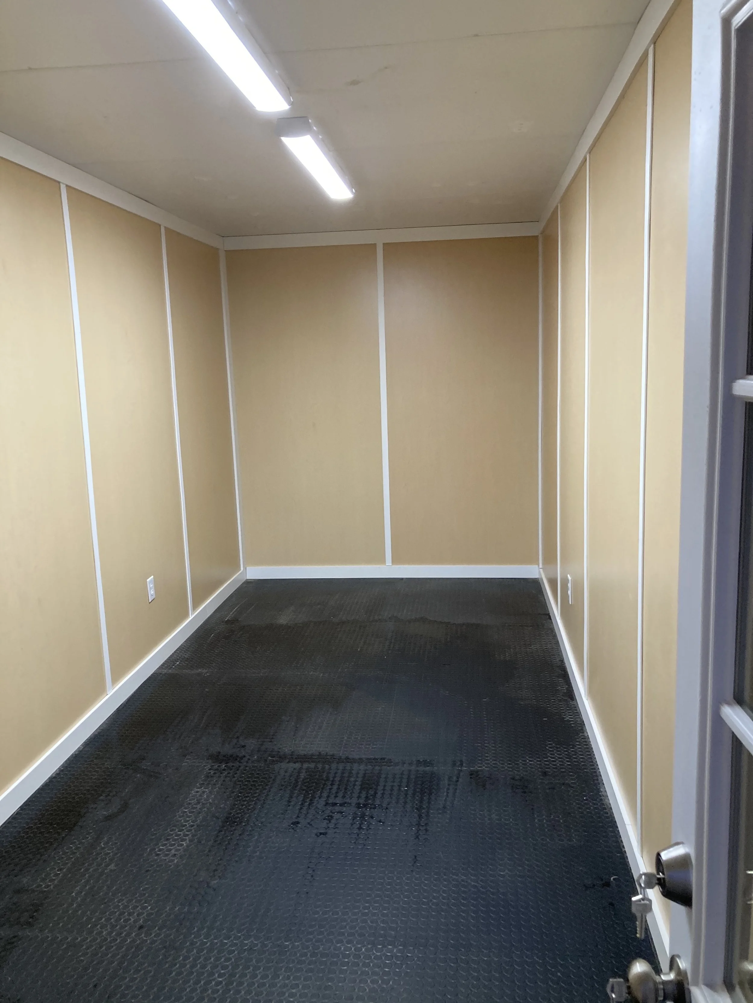 Empty room with beige walls, white trim, black rubber flooring, and fluorescent ceiling lights.