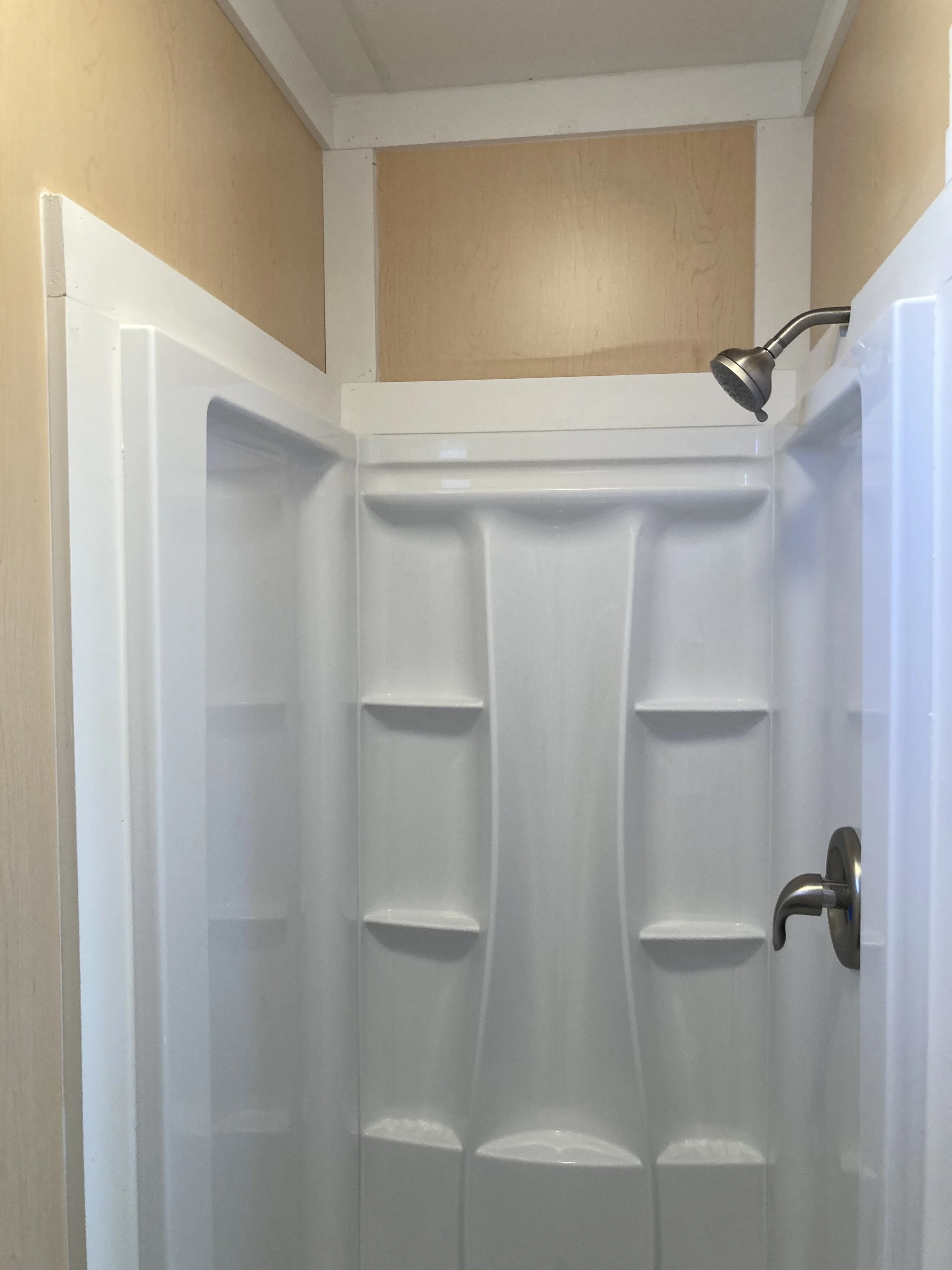 Interior of a small shower with white walls, showerhead, faucet, and built-in shelves.