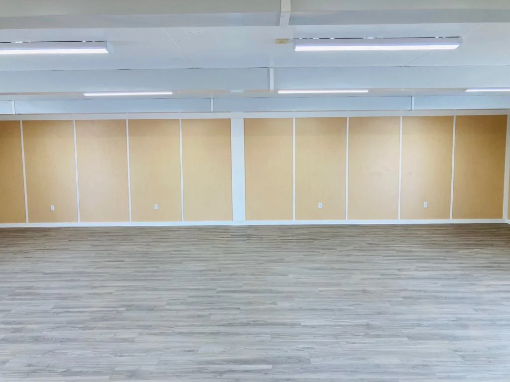 Empty room with wooden floor, beige paneled walls, and ceiling lights.