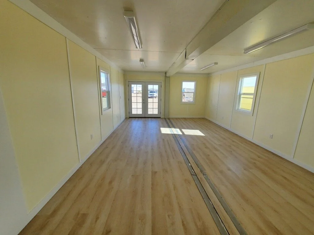 Empty room with wooden floors, yellow walls, white trim, and multiple windows with sunlight streaming in.