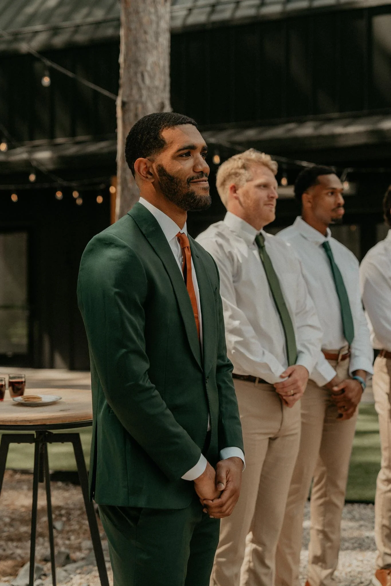 A man in a green suit and orange tie standing with others dressed in white shirts and green ties at an outdoor event.