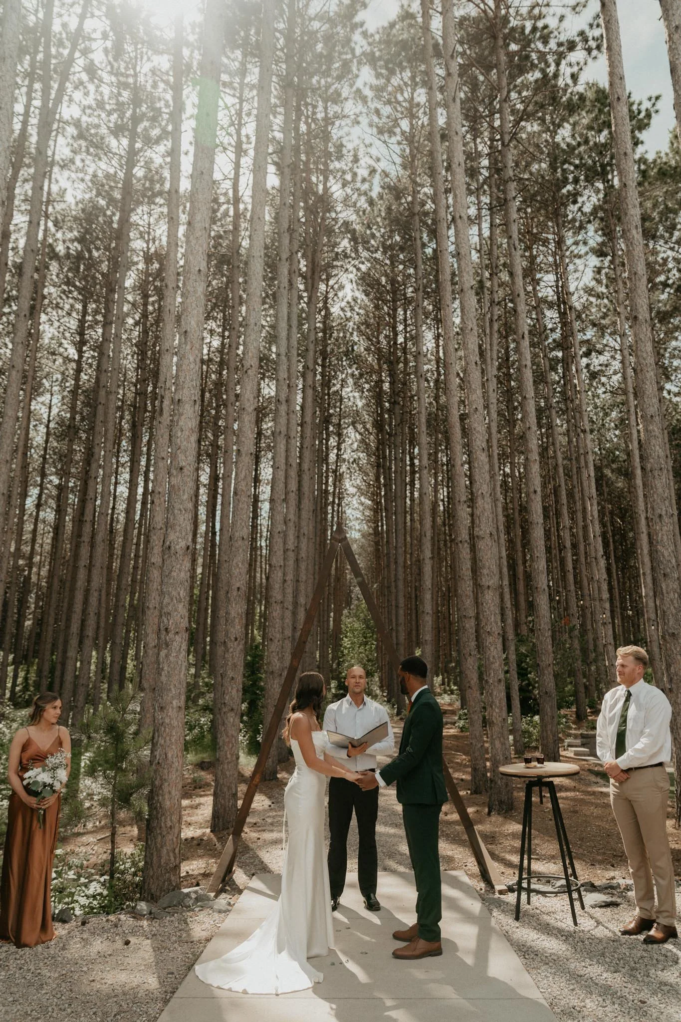A couple gets married outdoors in a forest, with an officiant and two witnesses present.