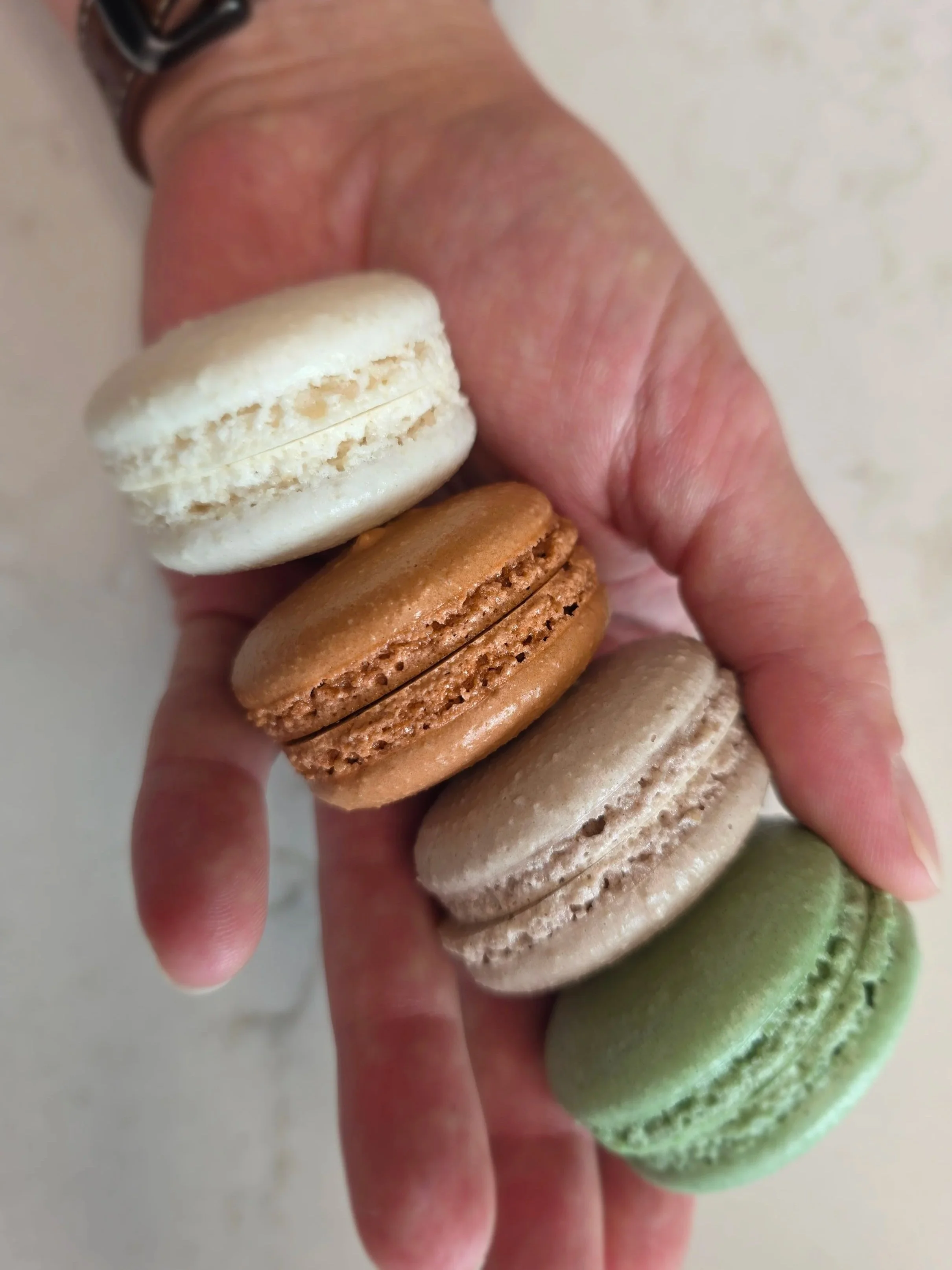 A hand holding four colorful macarons in a vertical line.